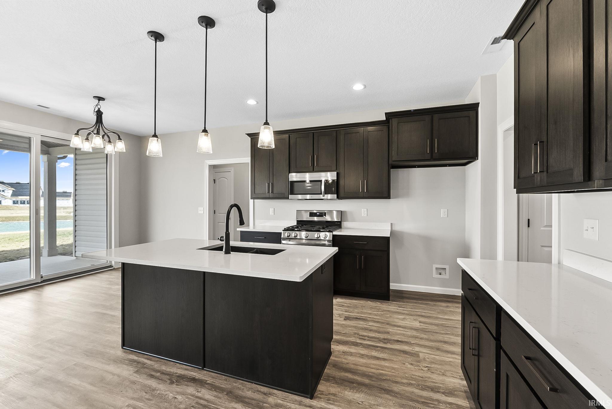Kitchen featuring stainless steel appliances, dark wood finished floors, light stone counters, an island with sink, and a chandelier