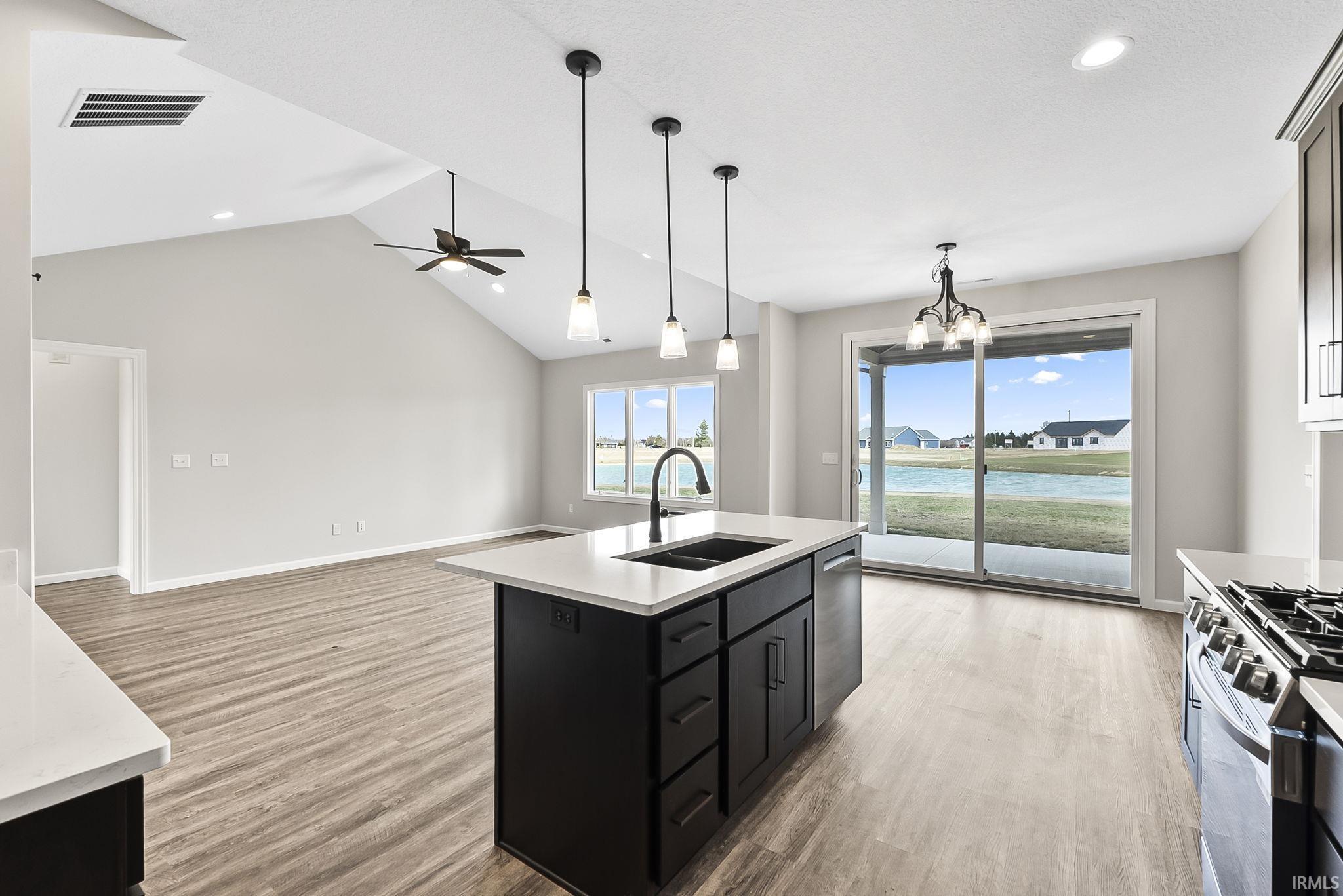 Kitchen with dark cabinetry, open floor plan, a chandelier, light wood-type flooring, and a kitchen island with sink
