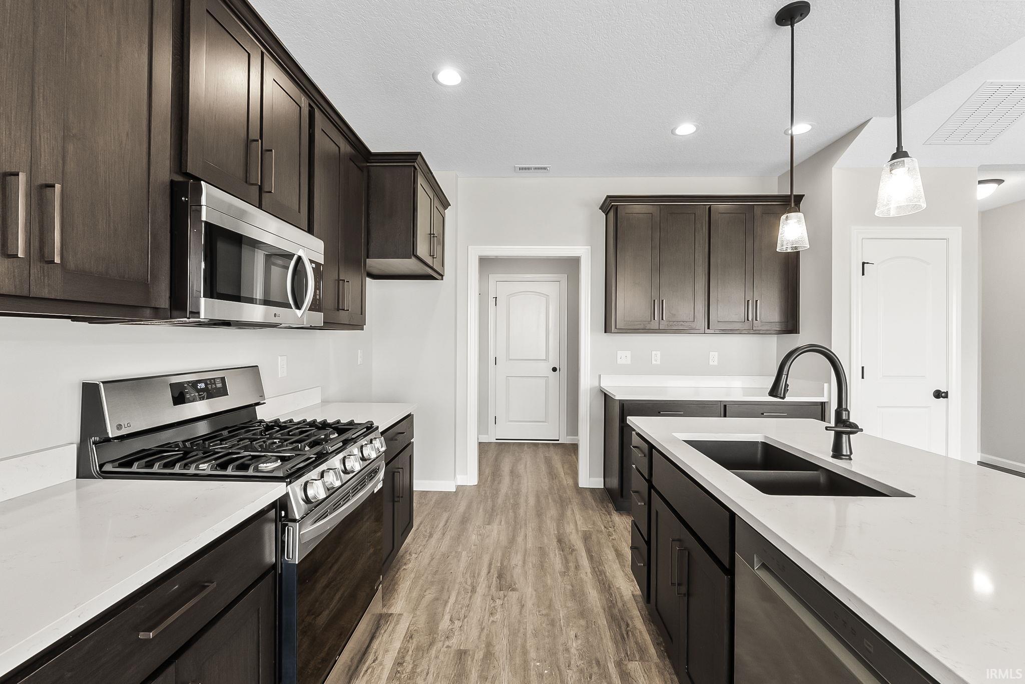 Kitchen with stainless steel appliances, dark wood finish cabinetry, light stone counters, light wood-style flooring, and pendant lighting