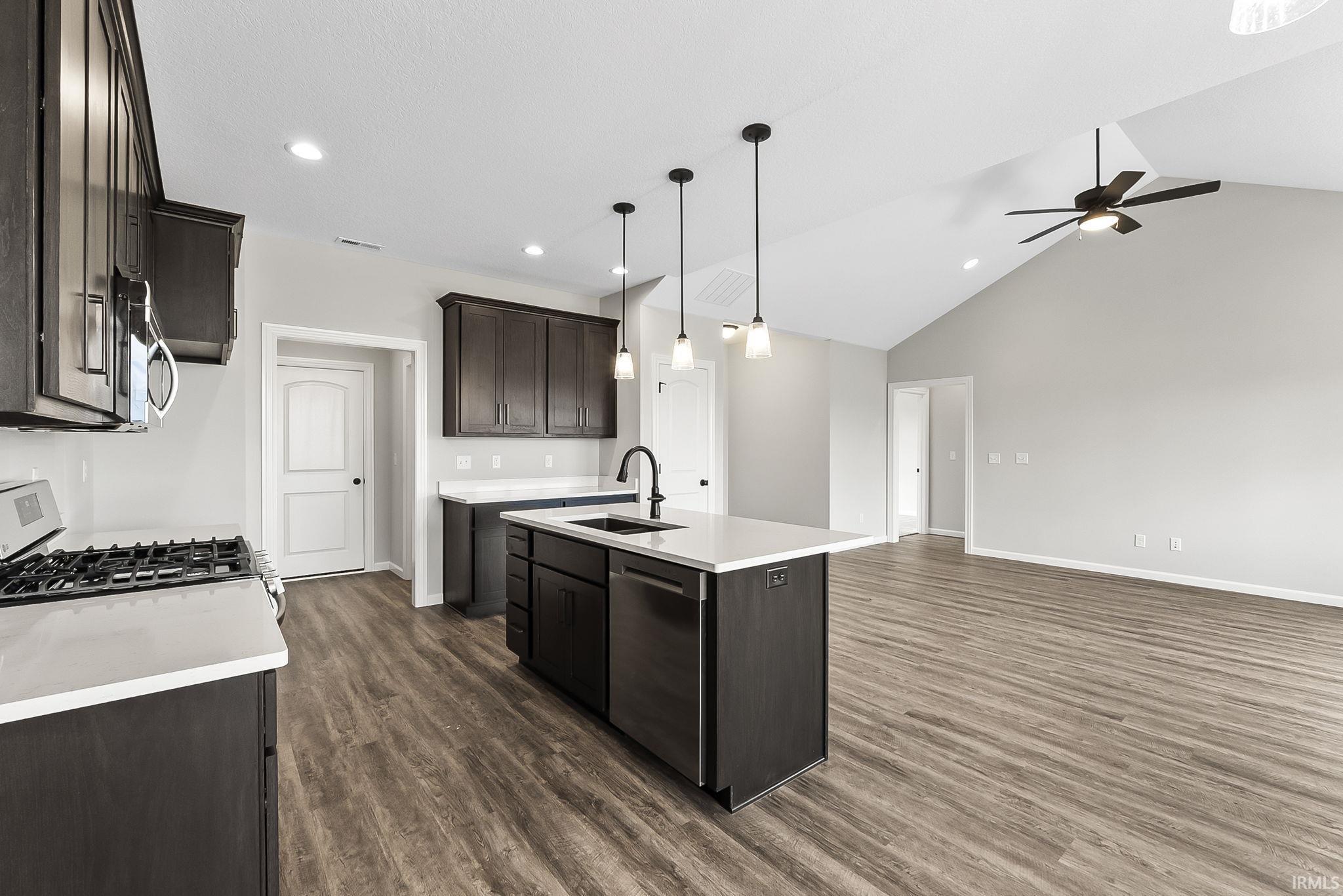 Kitchen with a kitchen island with sink, pendant lighting, dark wood finish cabinets, stainless steel appliances, and lofted ceiling