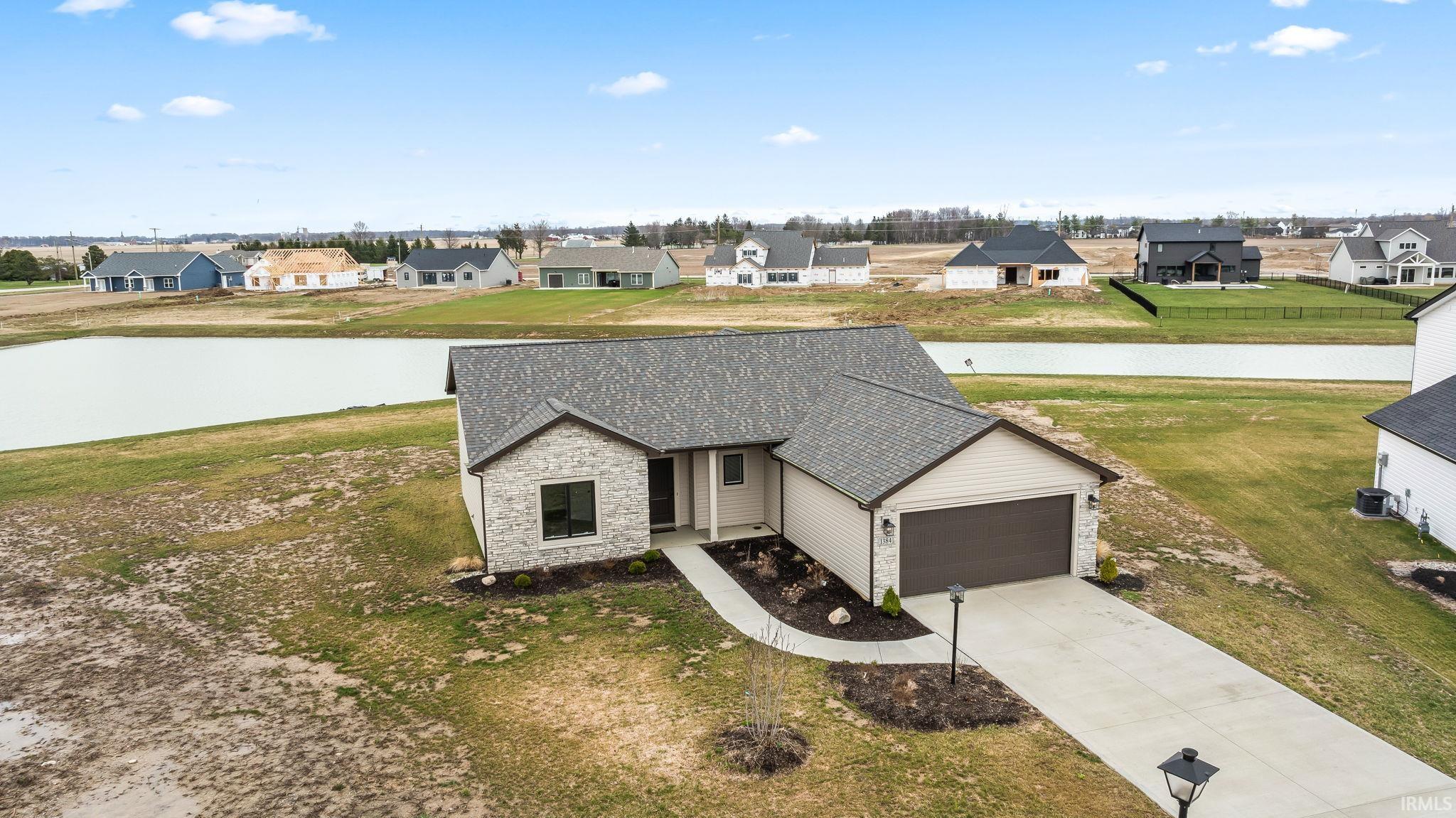 Traditional home with driveway, stone siding, an attached garage, a residential view, and a front lawn
