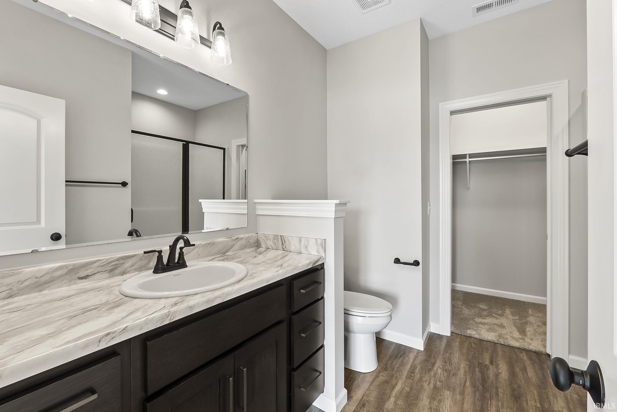 Bathroom featuring a stall shower, vanity, dark wood-type flooring, and a walk in closet