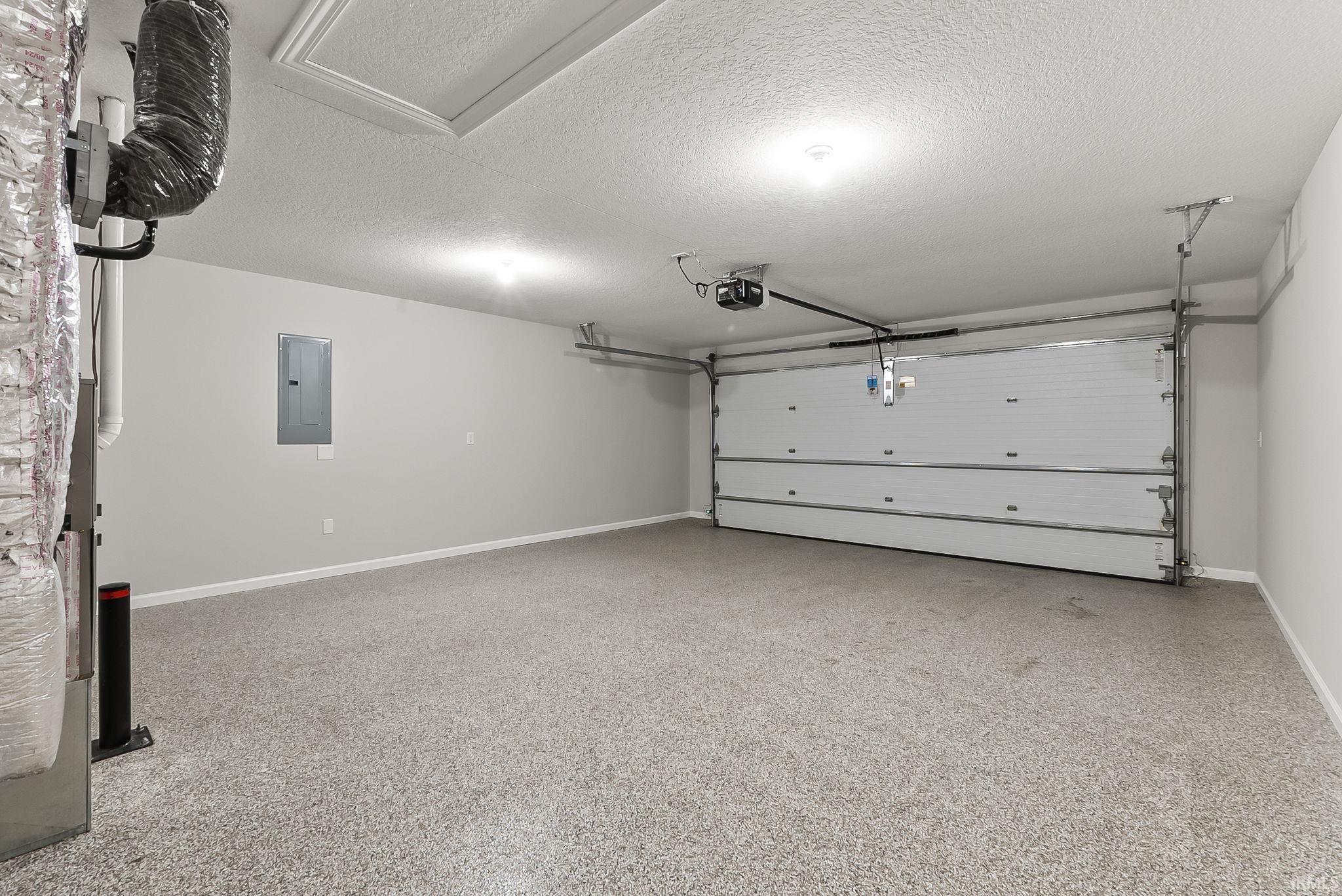 Garage featuring electric panel, heating unit, and a garage door opener
