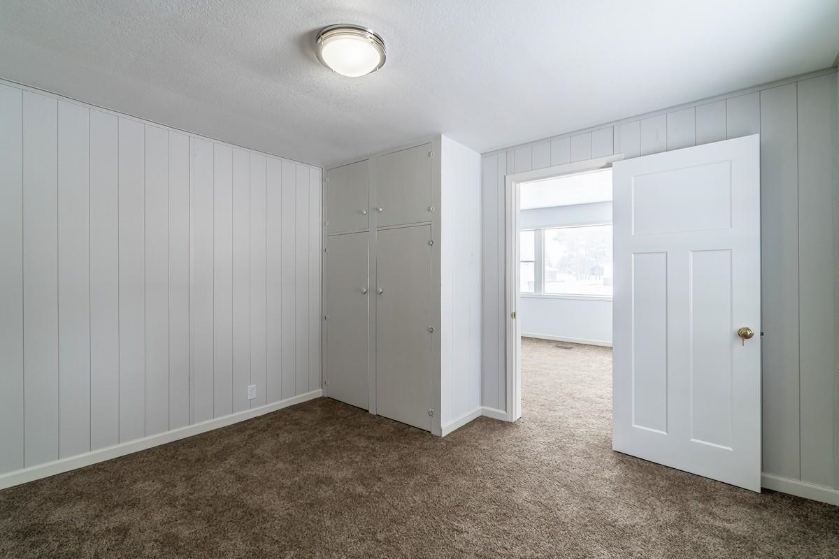 Unfurnished bedroom with wooden walls, dark carpet, a closet, and a textured ceiling
