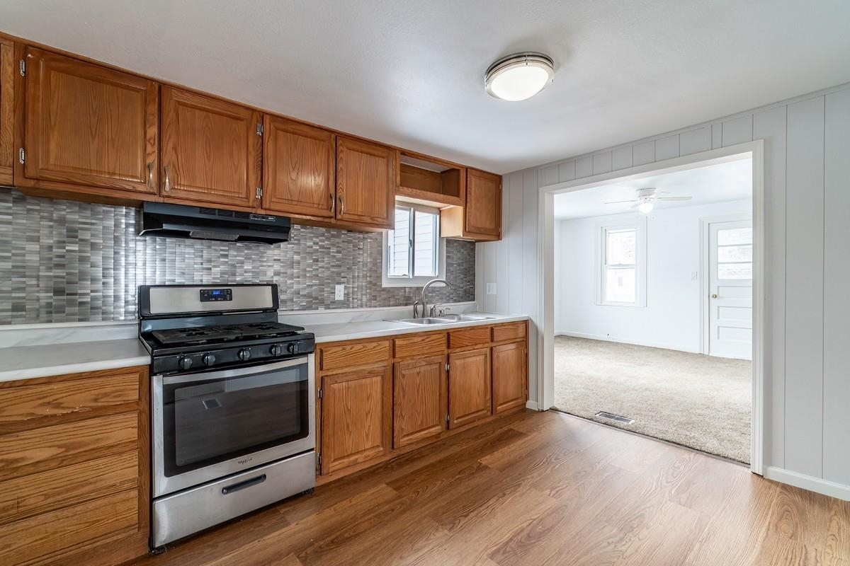 Kitchen with gas stove, light countertops, wood finish cabinets, and decorative backsplash