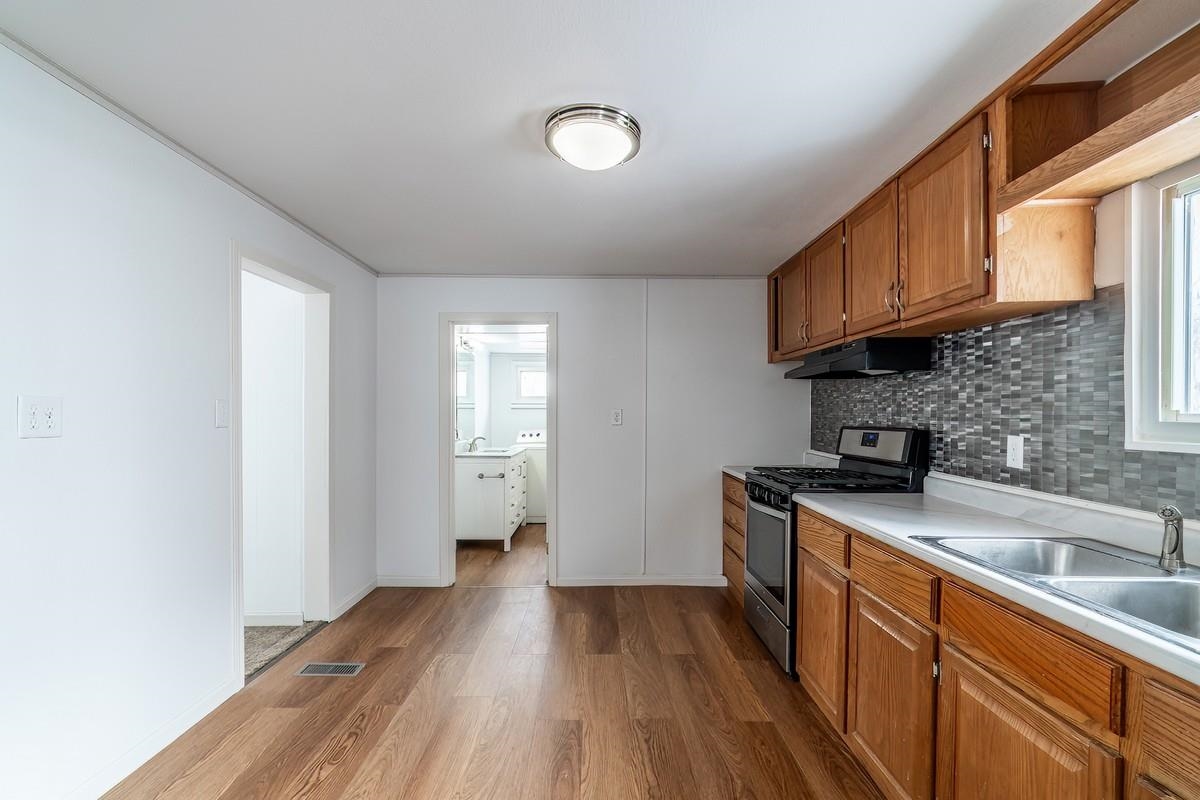 Kitchen featuring gas stove, light countertops, wood finish cabinets, dark wood-style flooring, and decorative backsplash