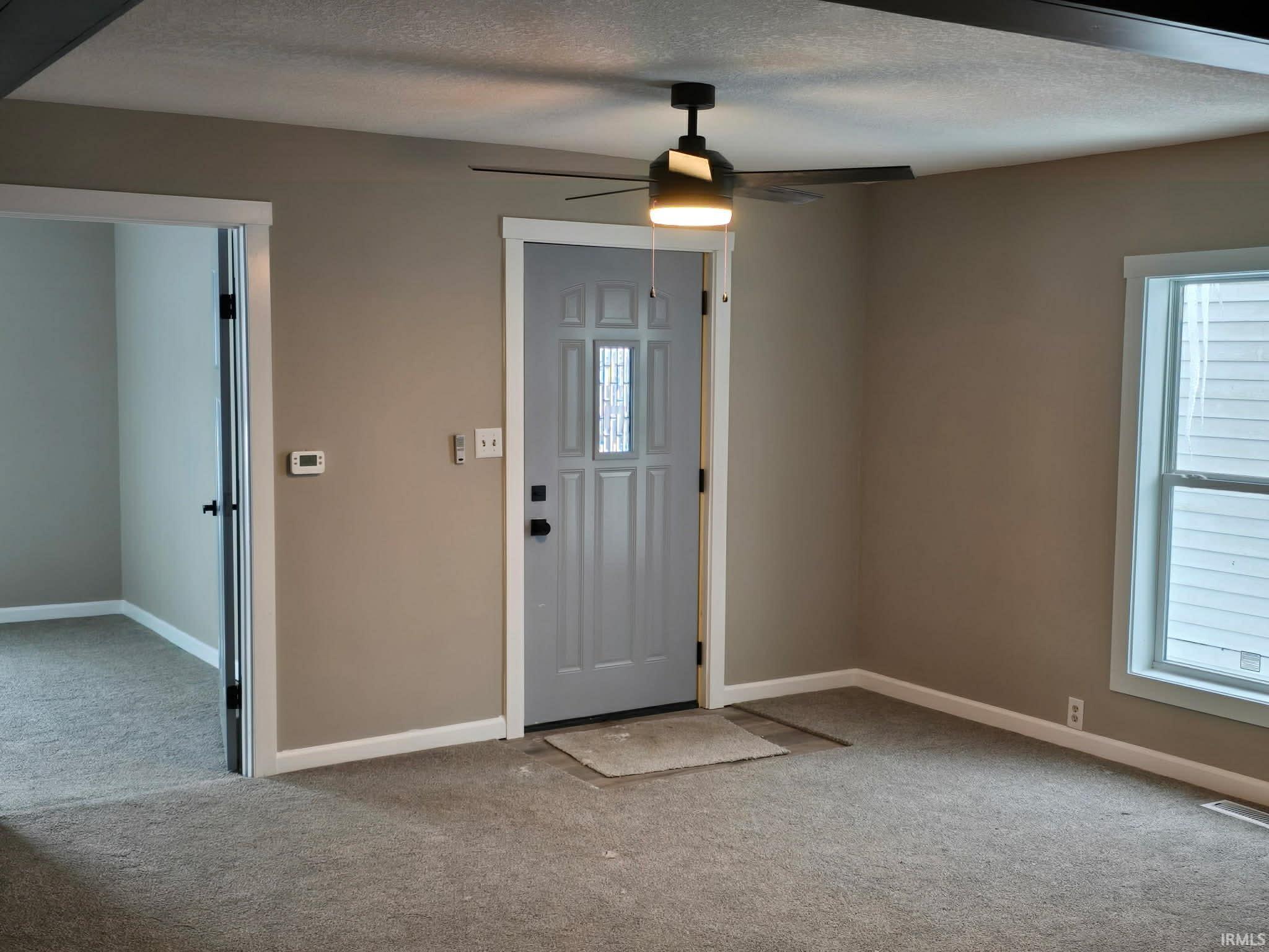 Entryway with light colored carpet, ceiling fan, and a textured ceiling