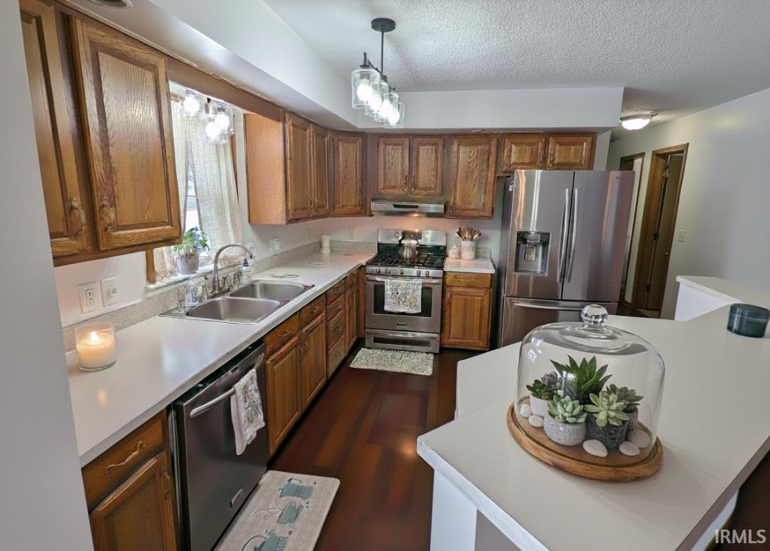 Kitchen featuring stainless steel appliances, light countertops, brown cabinets, decorative light fixtures, and a textured ceiling