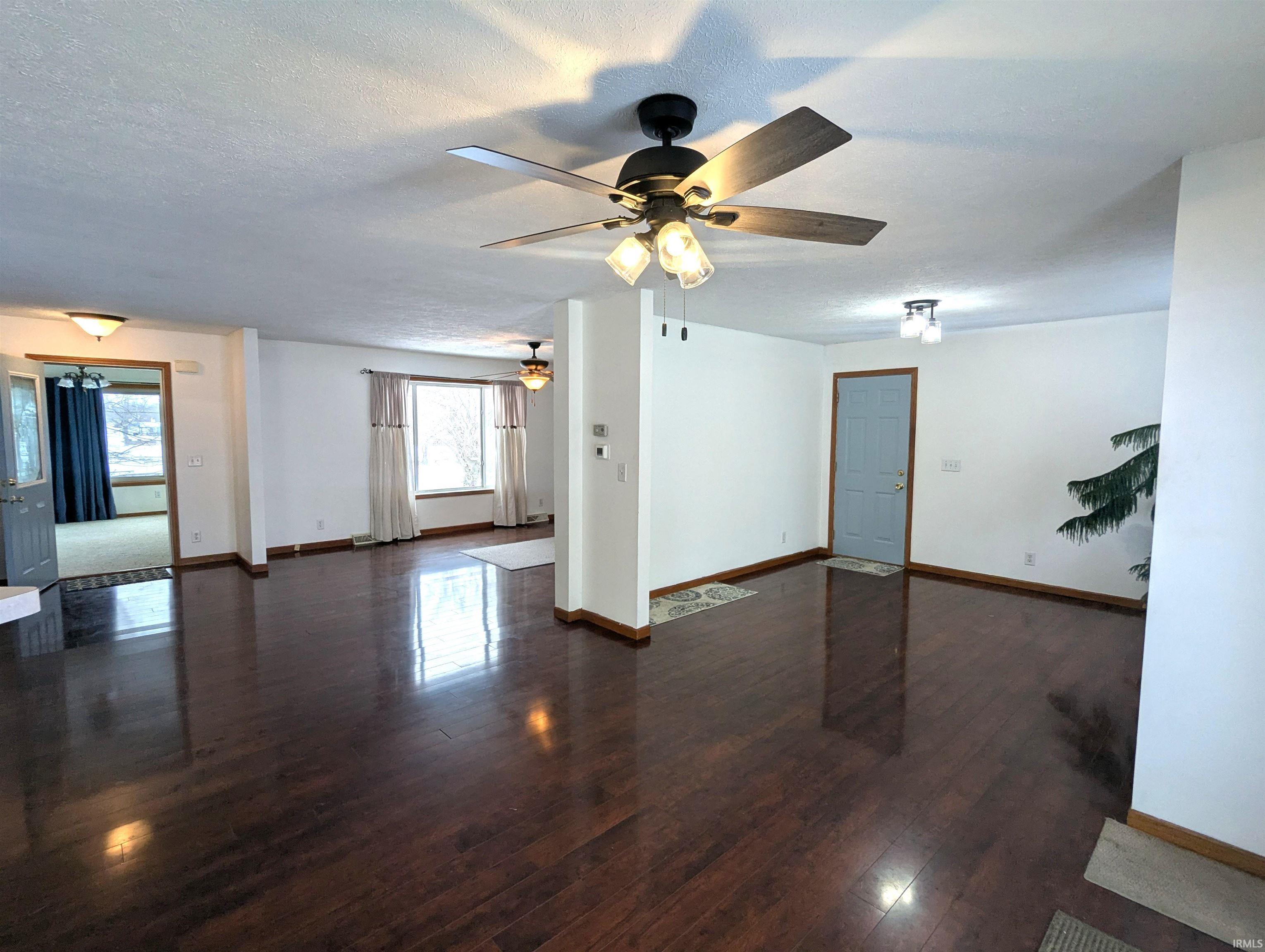 Unfurnished living room/dining room featuring dark wood-style floors, a textured ceiling, and ceiling fan