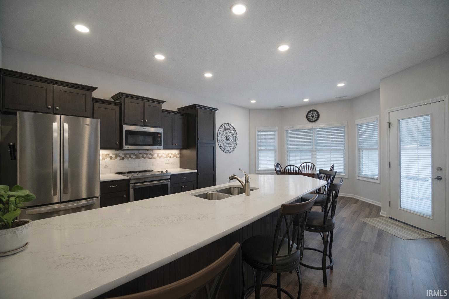 Kitchen with stainless steel appliances, dark wood-type flooring, backsplash, a breakfast bar, and light stone countertops