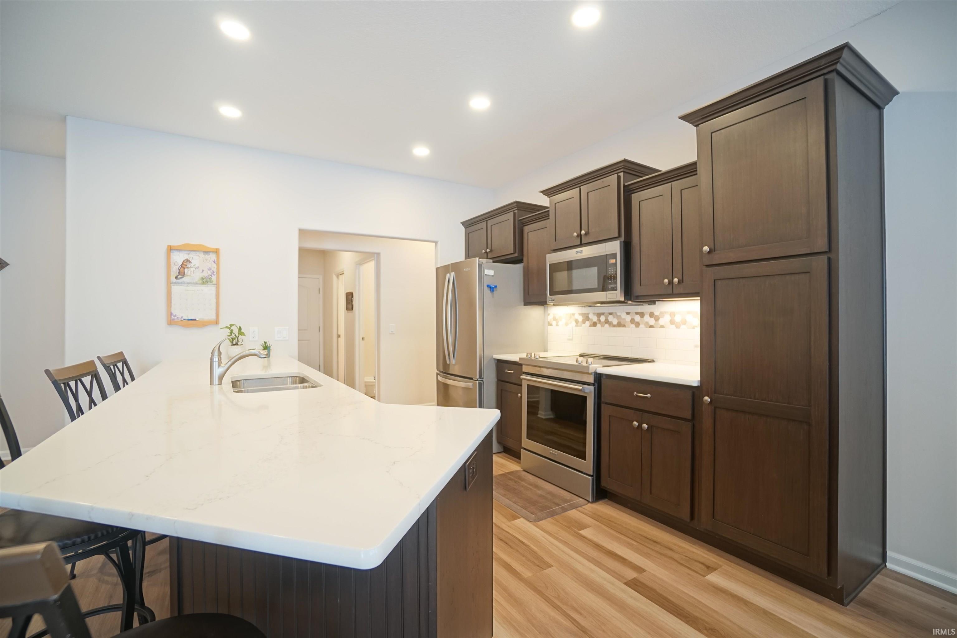 Kitchen featuring a breakfast bar, stainless steel appliances, light wood-style flooring, dark wood finish cabinetry, and recessed lighting
