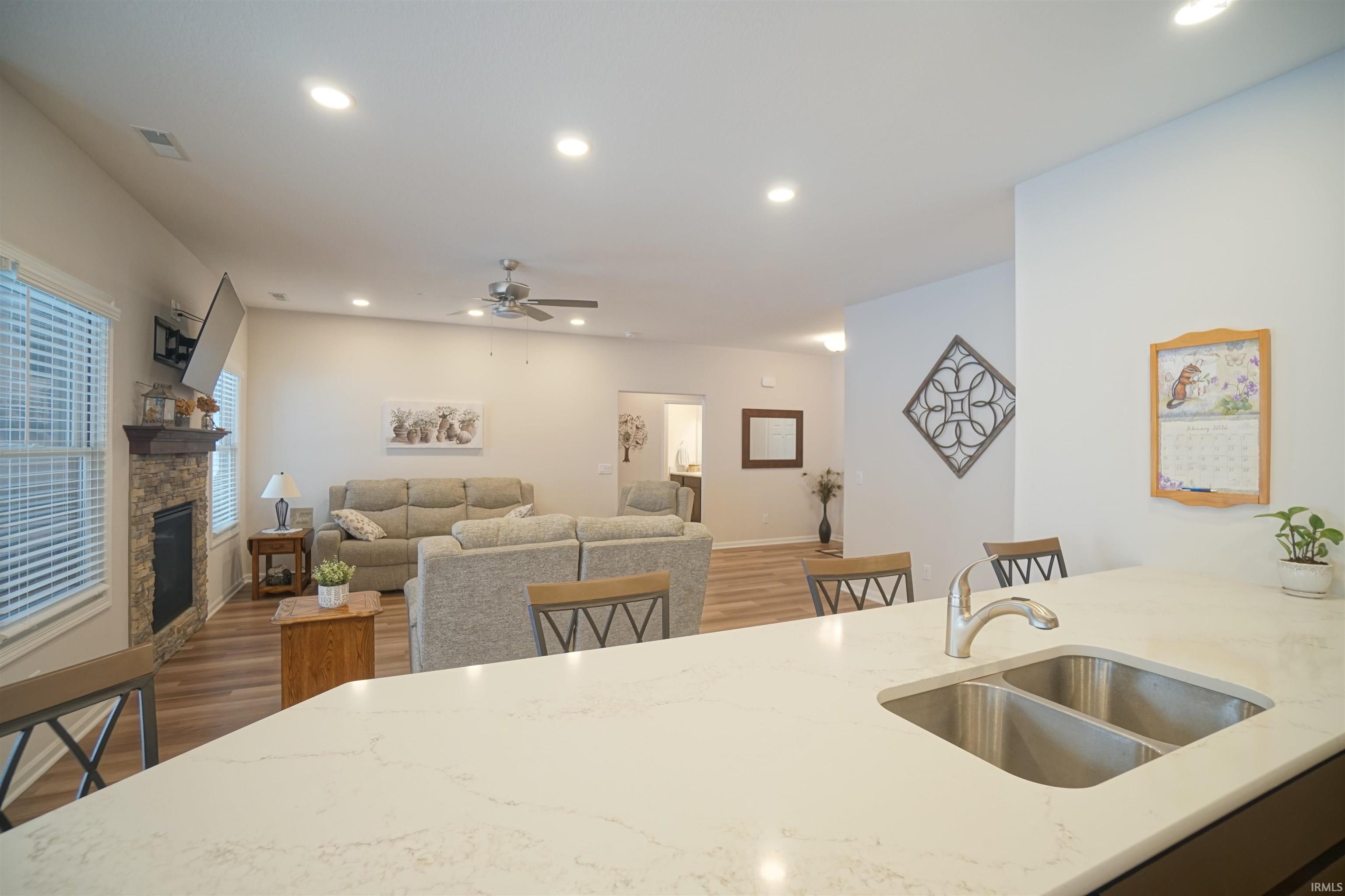 Kitchen featuring wood finished floors, recessed lighting, light stone counters, a breakfast bar area, and a stone fireplace