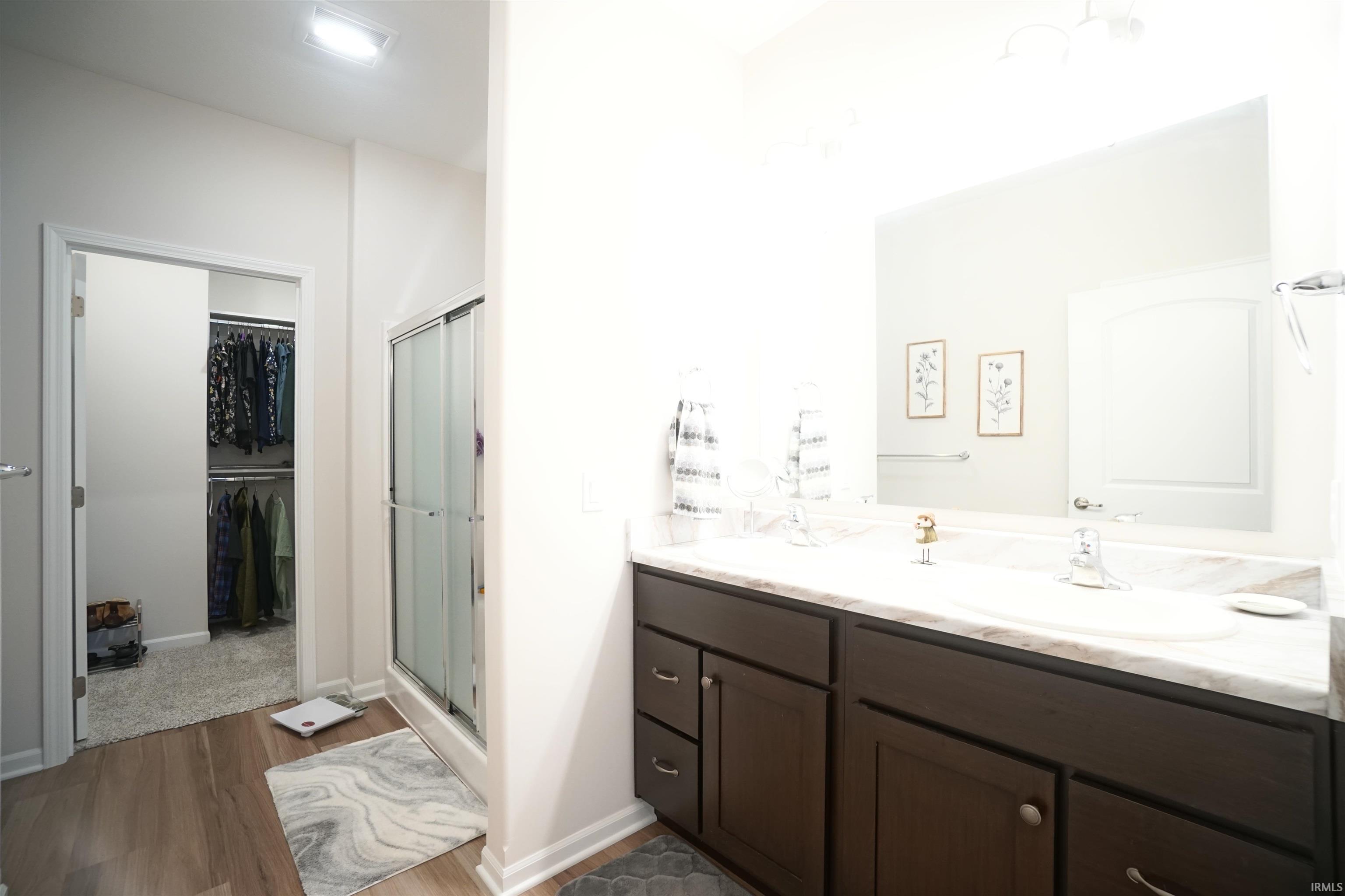 Bathroom with a stall shower, double vanity, a walk in closet, and dark wood-style flooring
