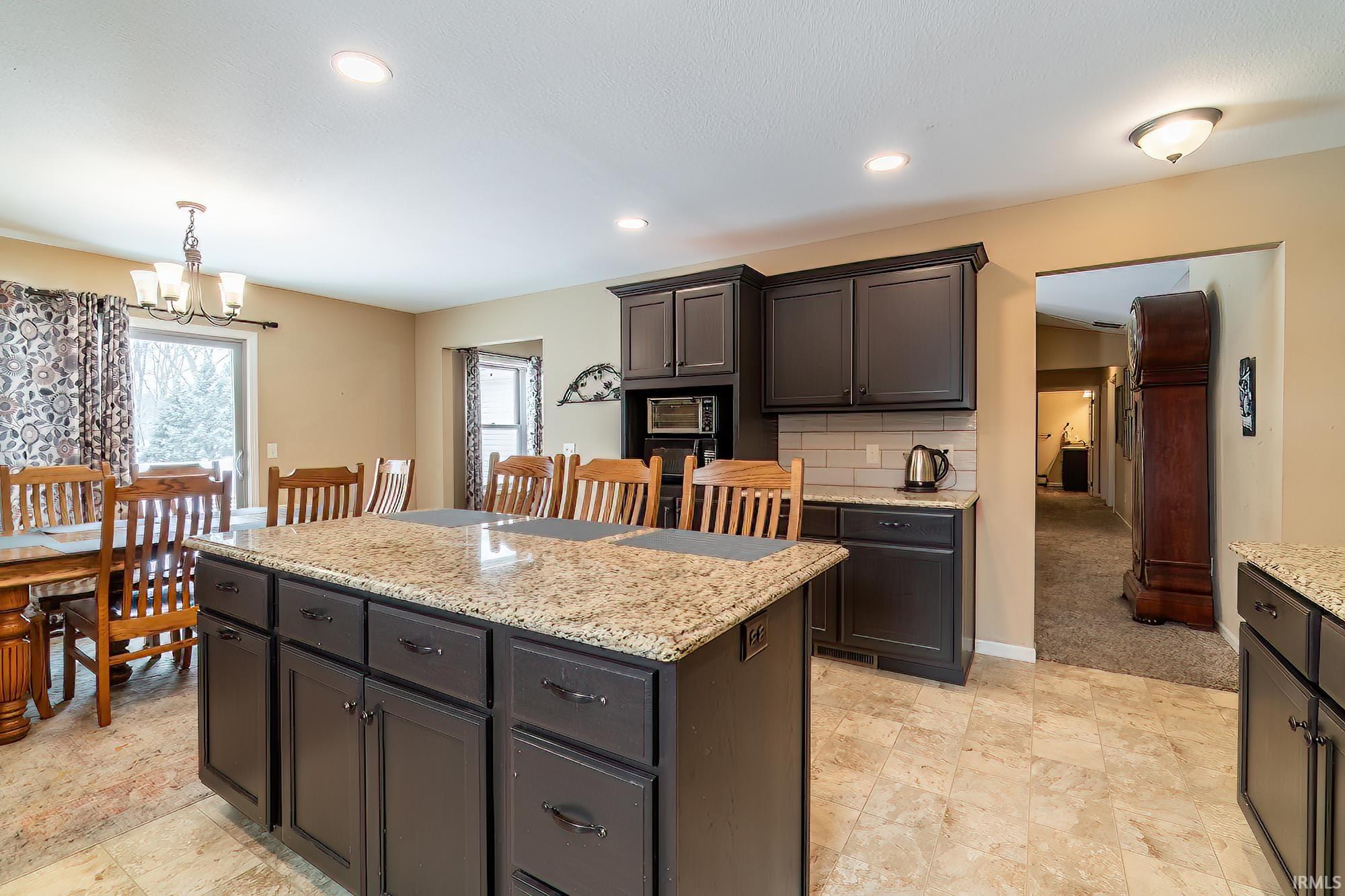 Kitchen with decorative backsplash, light stone countertops, suspended lighting, and a kitchen island