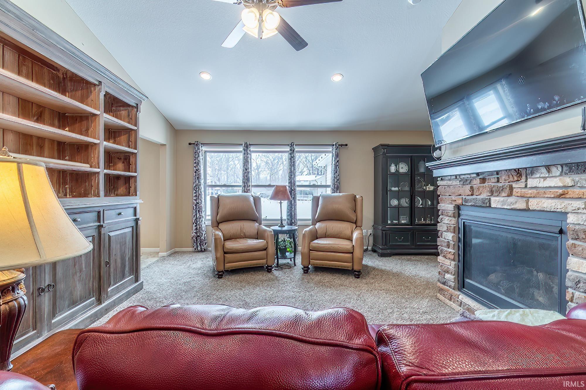 Living room featuring ceiling fan, a fireplace, lofted ceiling, and carpet