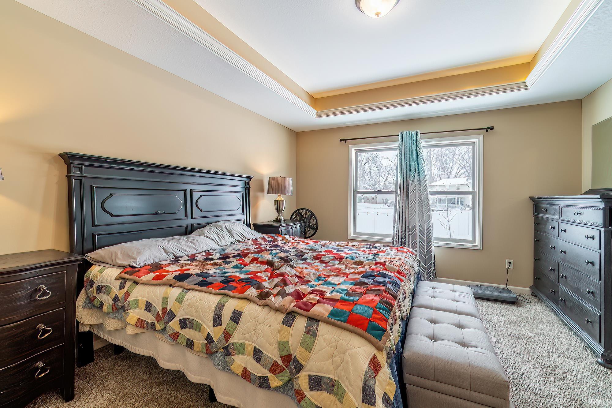 Carpeted bedroom with a raised ceiling and ornamental molding