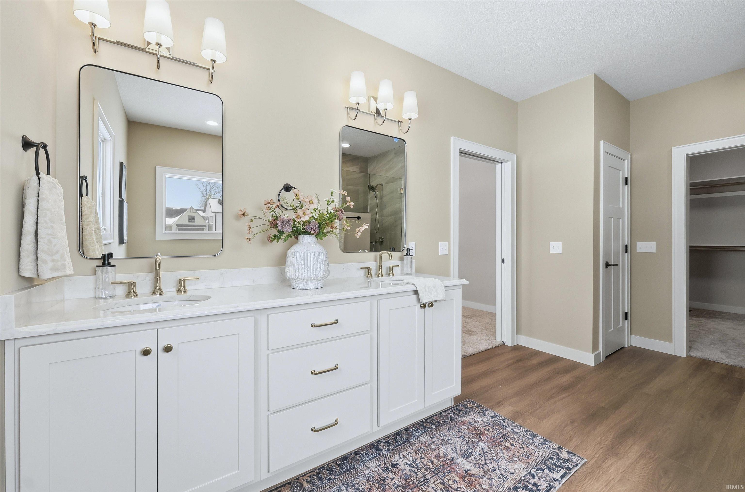 Full bathroom featuring a stall shower, a walk in closet, double vanity, and dark wood-style floors