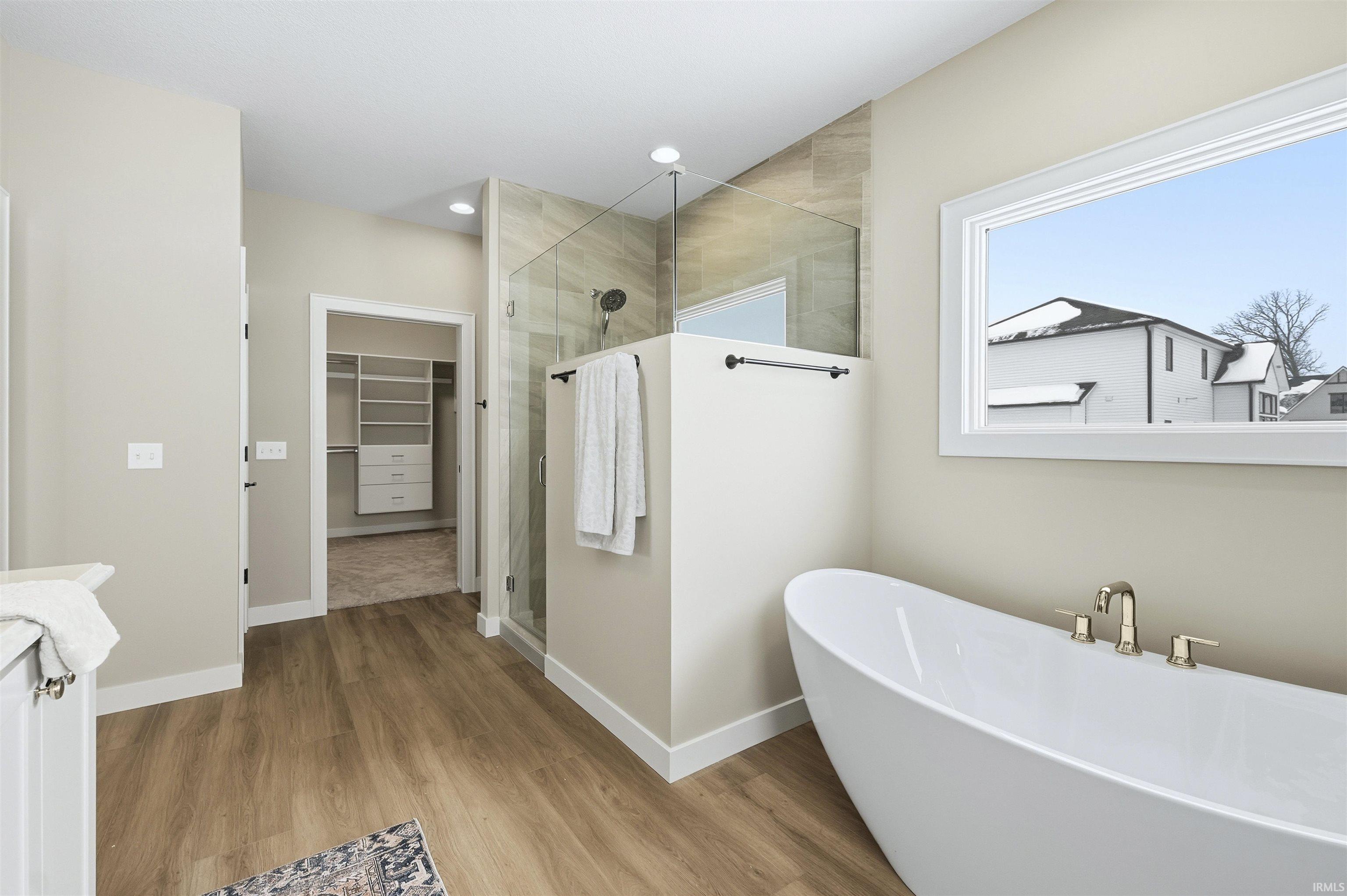 Full bathroom with a walk in closet, walk in shower, a freestanding tub, and light wood-style flooring