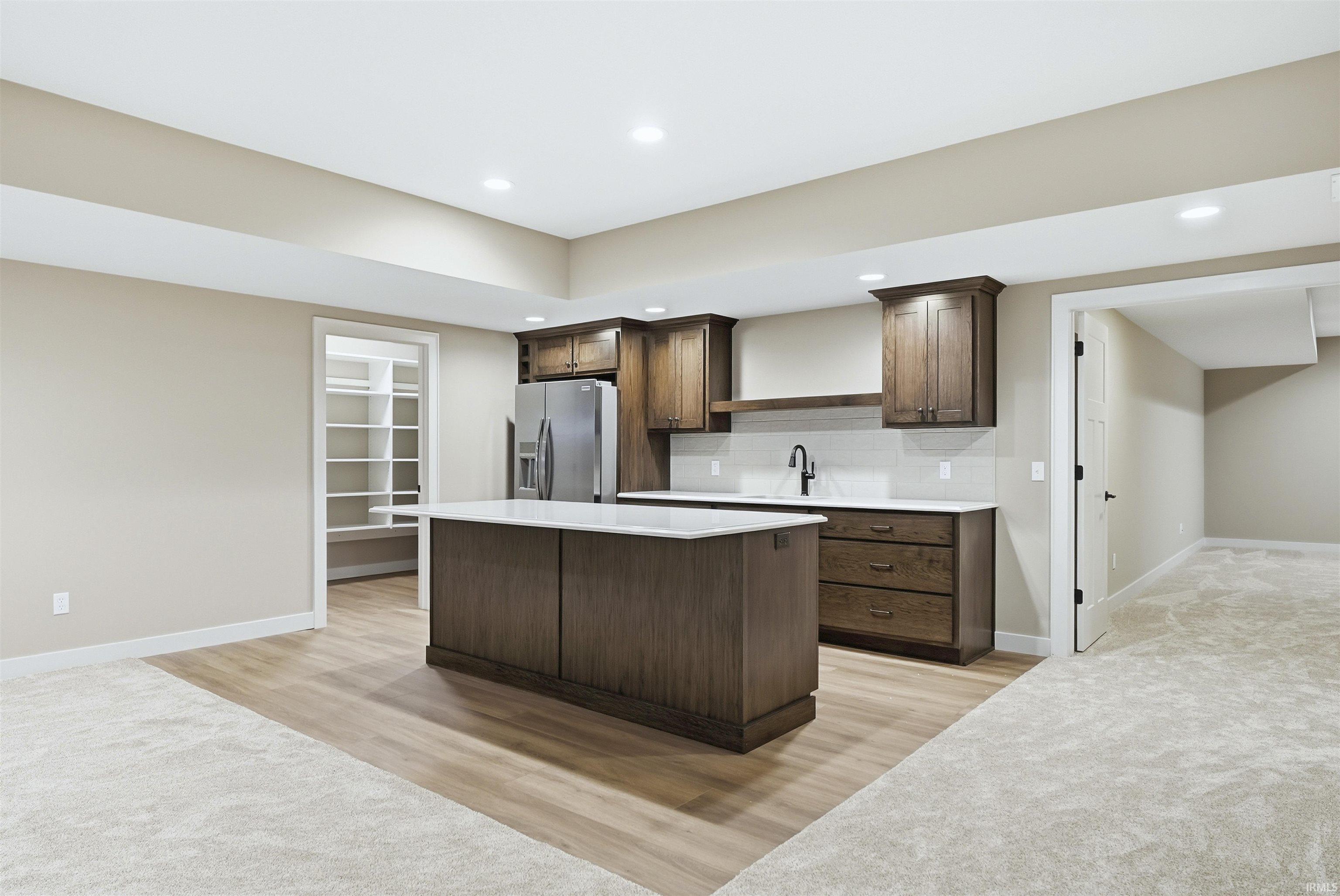 Kitchen with dark wood finish cabinetry, stainless steel refrigerator with ice dispenser, light wood-style floors, a kitchen island, and recessed lighting