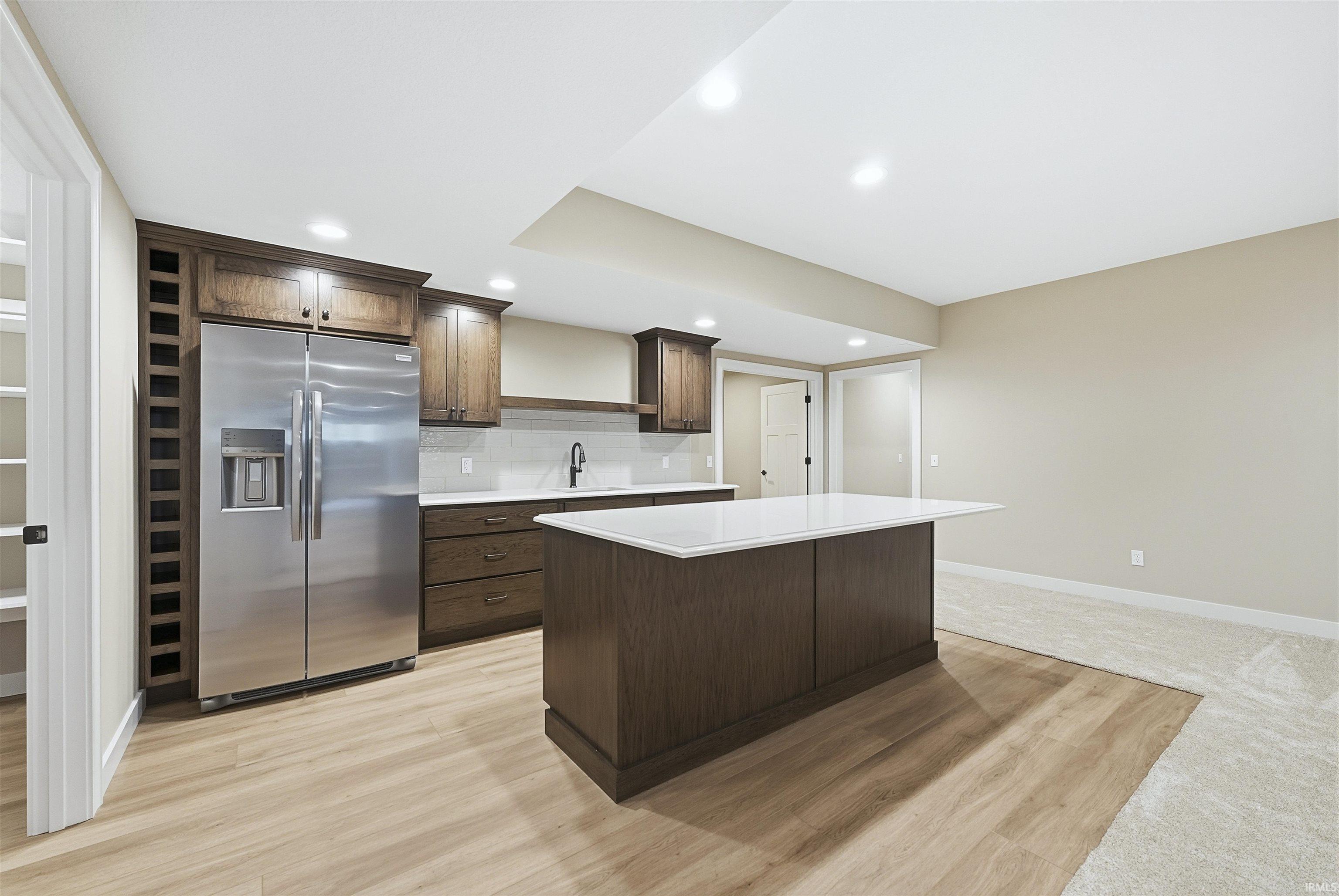 Kitchen with stainless steel refrigerator with ice dispenser, dark wood finish cabinets, light wood-type flooring, backsplash, and a center island