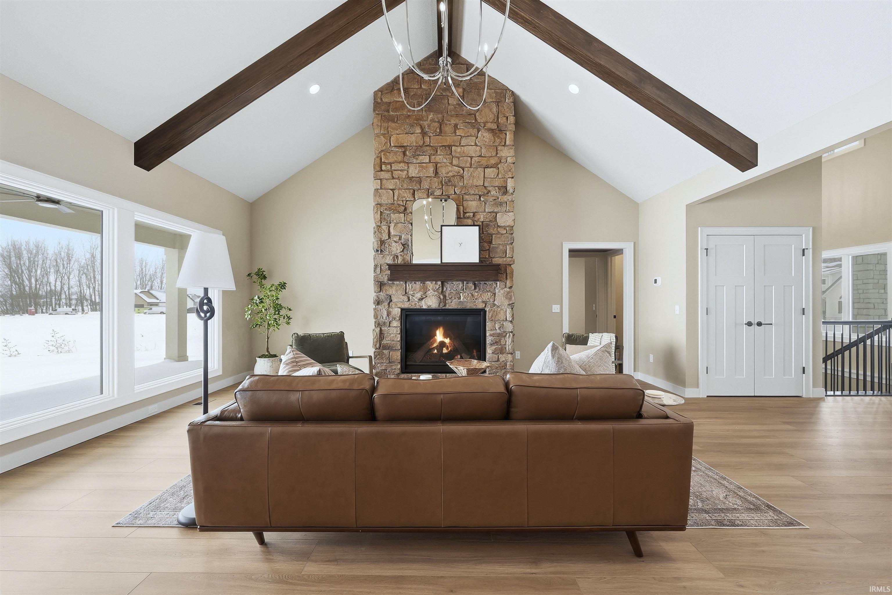 Living room with light wood-style flooring, a stone fireplace, and suspended lighting