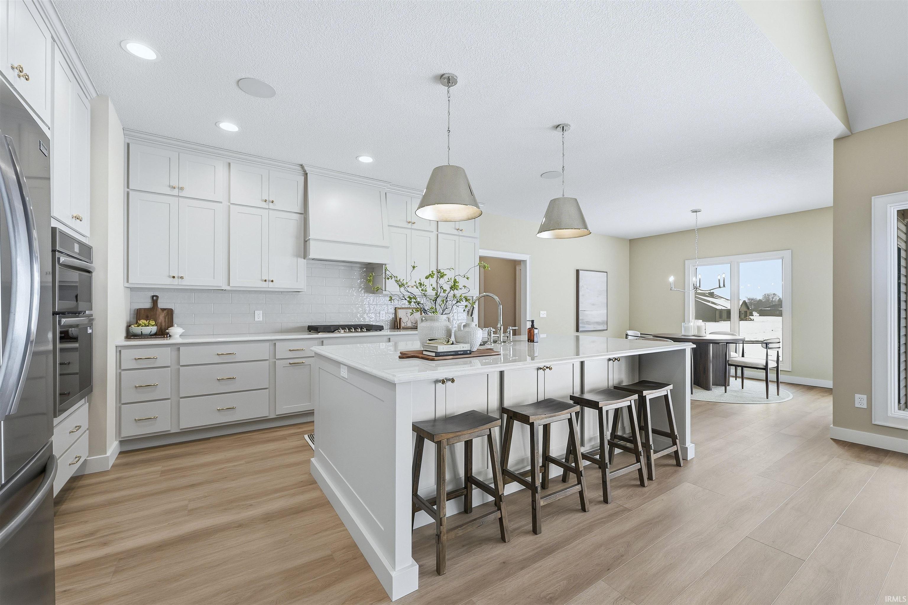 Kitchen with a kitchen bar, decorative light fixtures, an island with sink, and light wood-type flooring