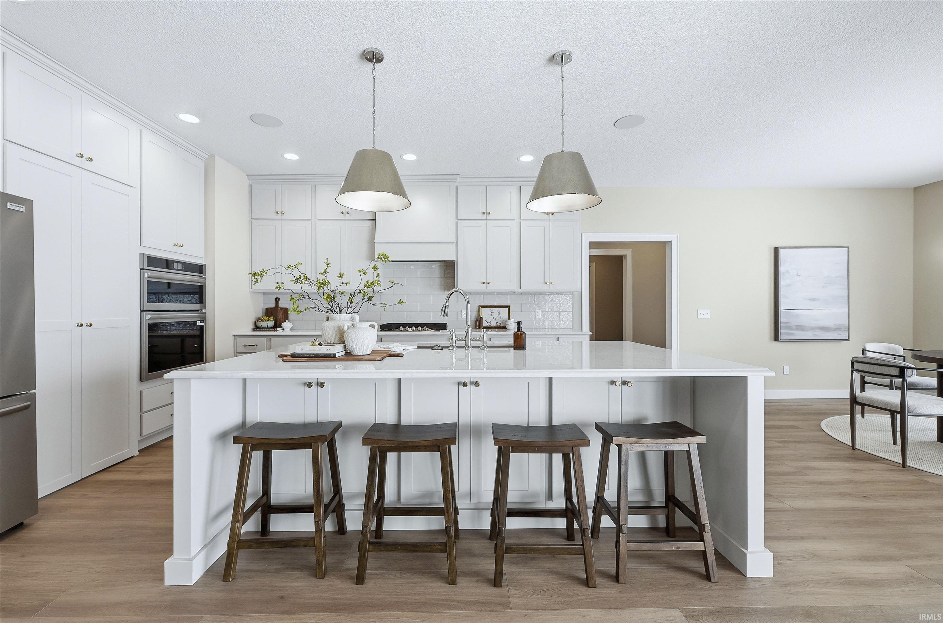 Kitchen with a kitchen breakfast bar, pendant lighting, light wood-type flooring, white cabinets, and an island with sink