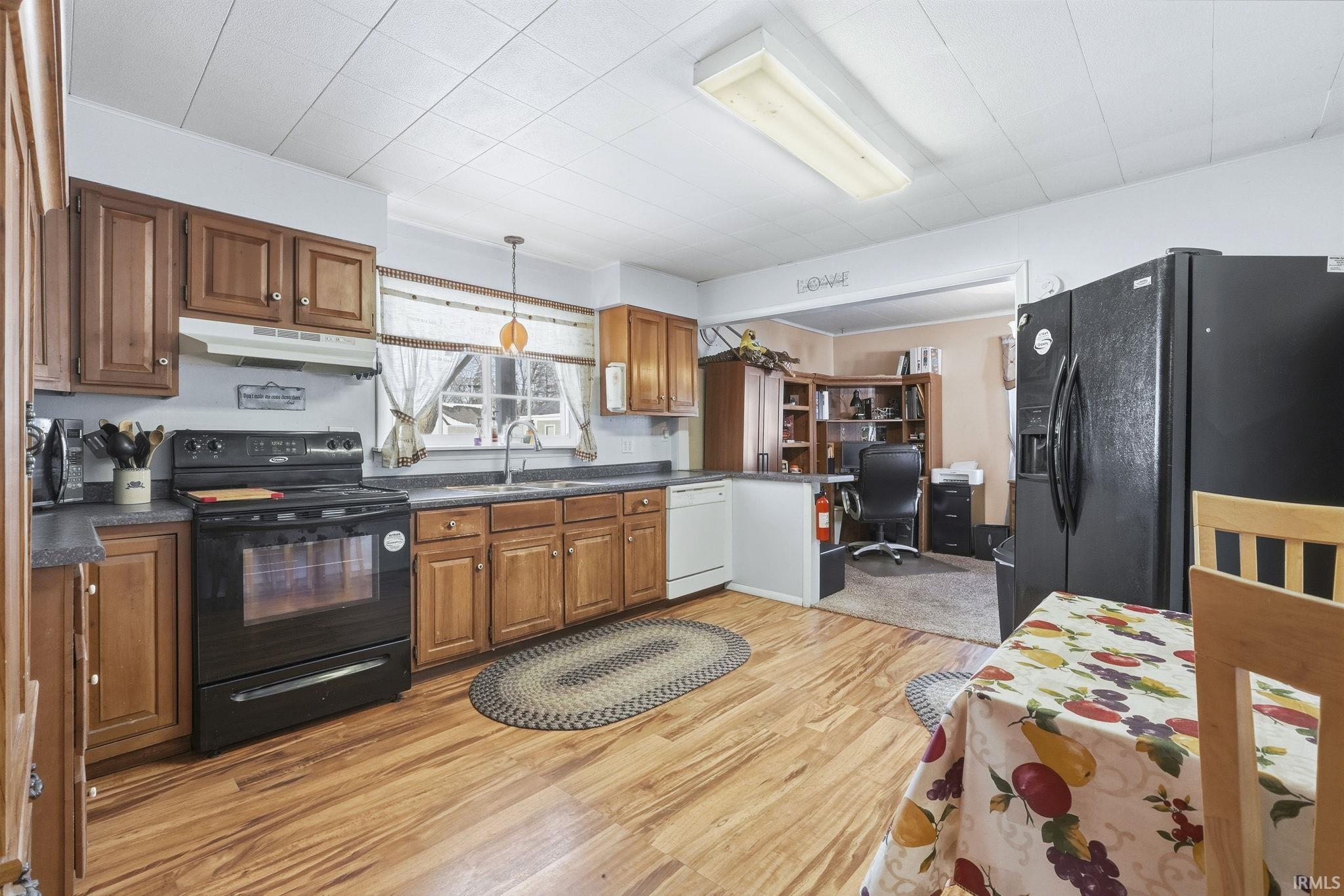 Kitchen with black appliances, wood finish cabinetry, dark countertops, a desk, and light wood-style floors