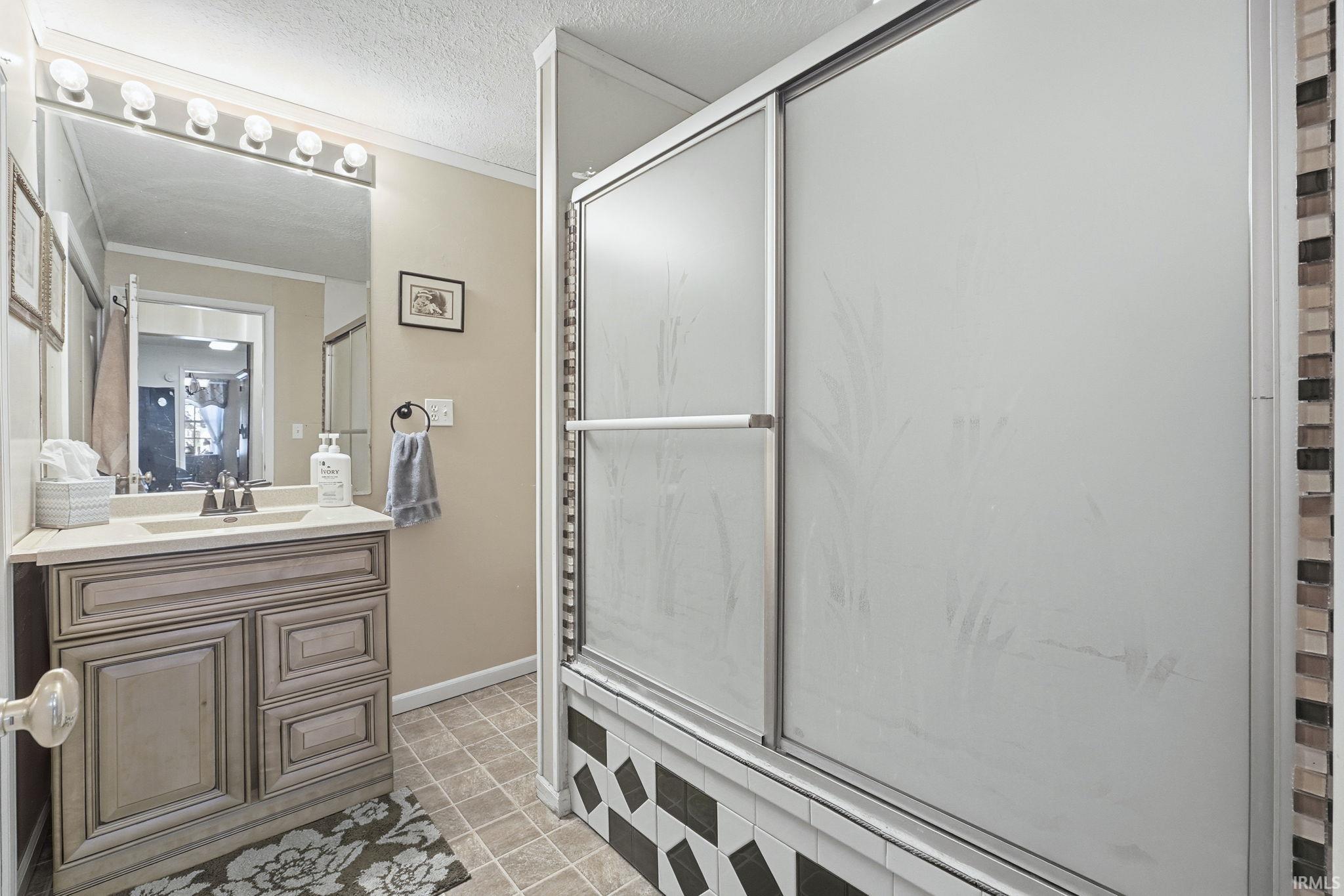 Bathroom featuring ornamental molding, vanity, light tile patterned flooring, a shower with door, and a textured ceiling