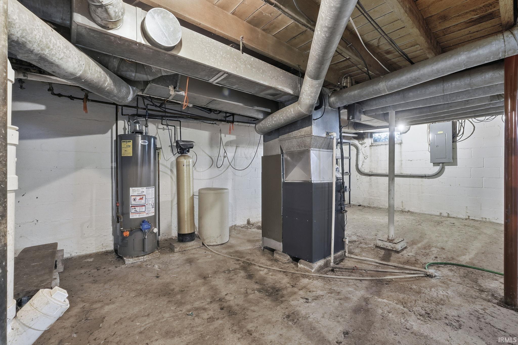 Unfinished basement featuring a water softener system, gas water heater, electric panel, and heating unit
