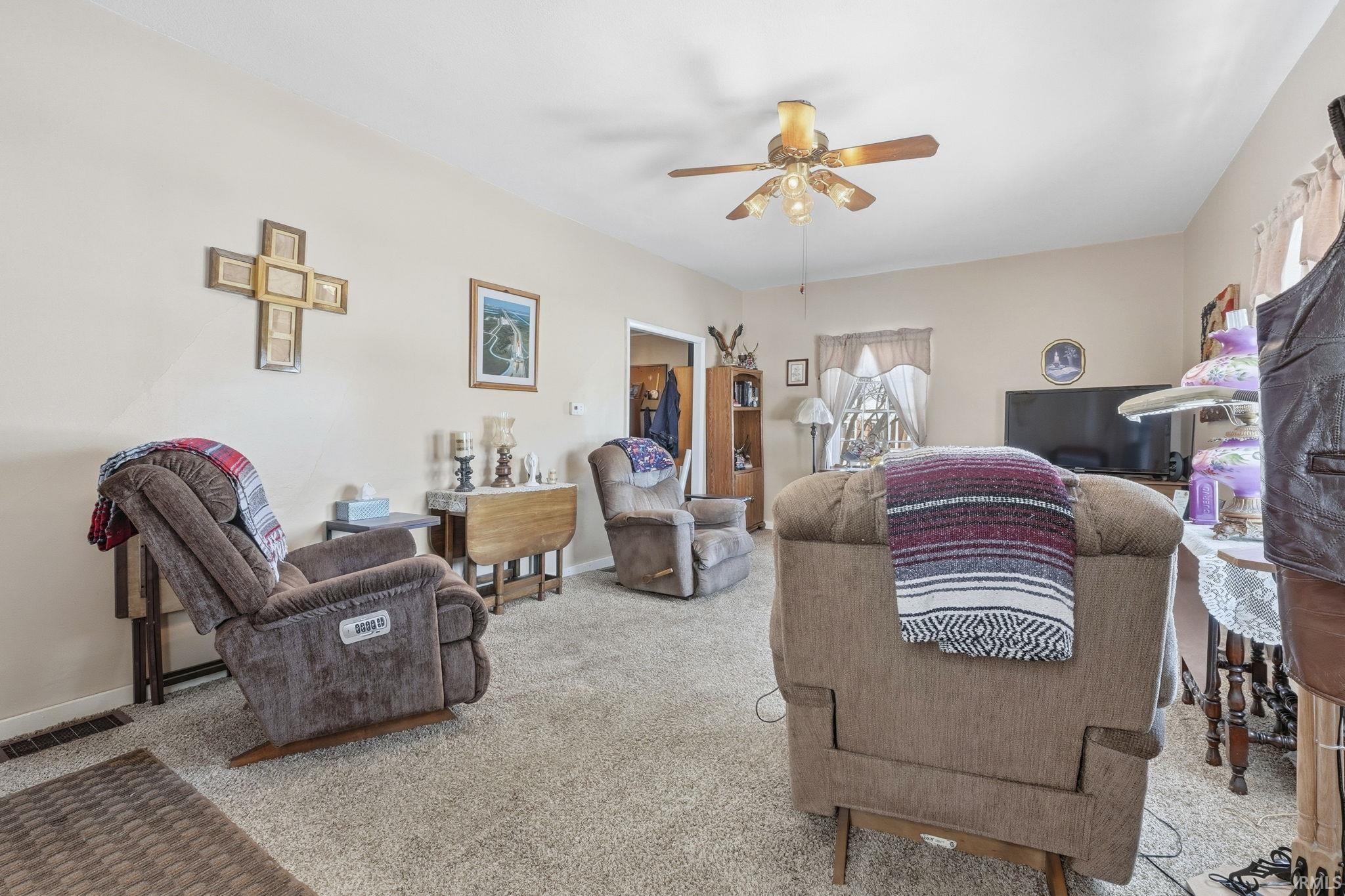 Carpeted living room featuring ceiling fan and baseboards