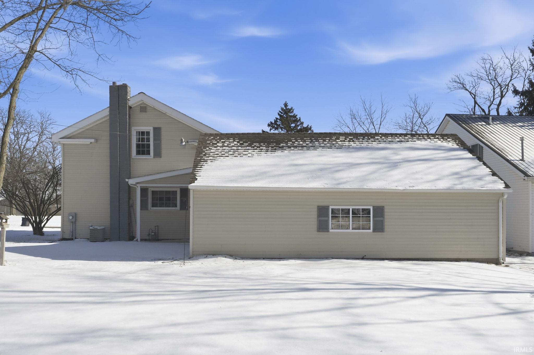 Snow covered property with a chimney and a central AC unit