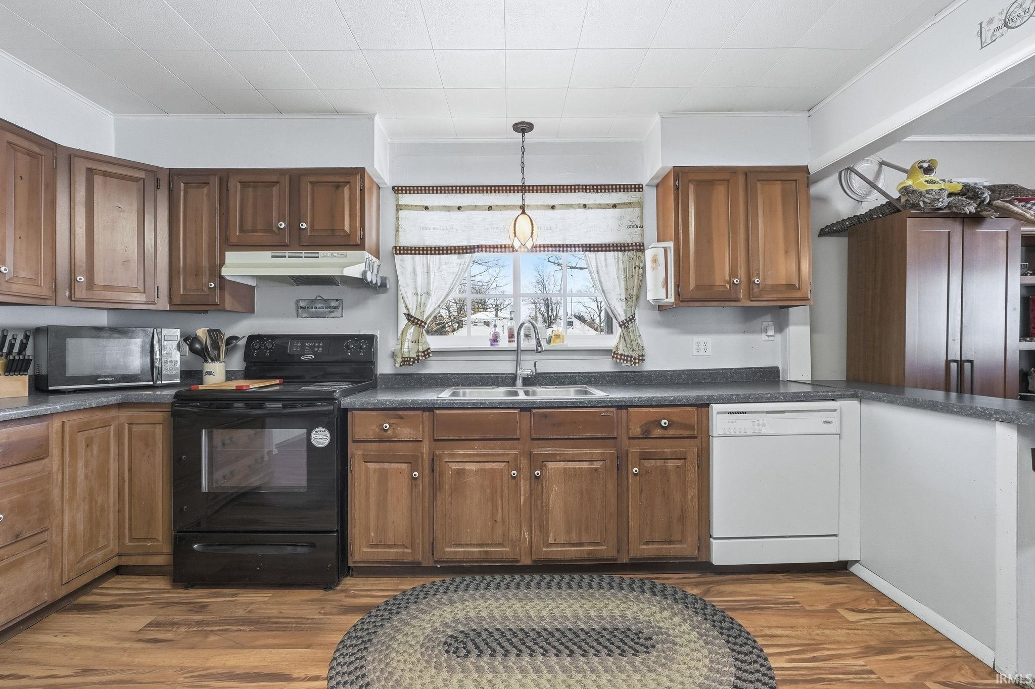 Kitchen with black appliances, crown molding, decorative light fixtures, dark wood-style flooring, and dark countertops