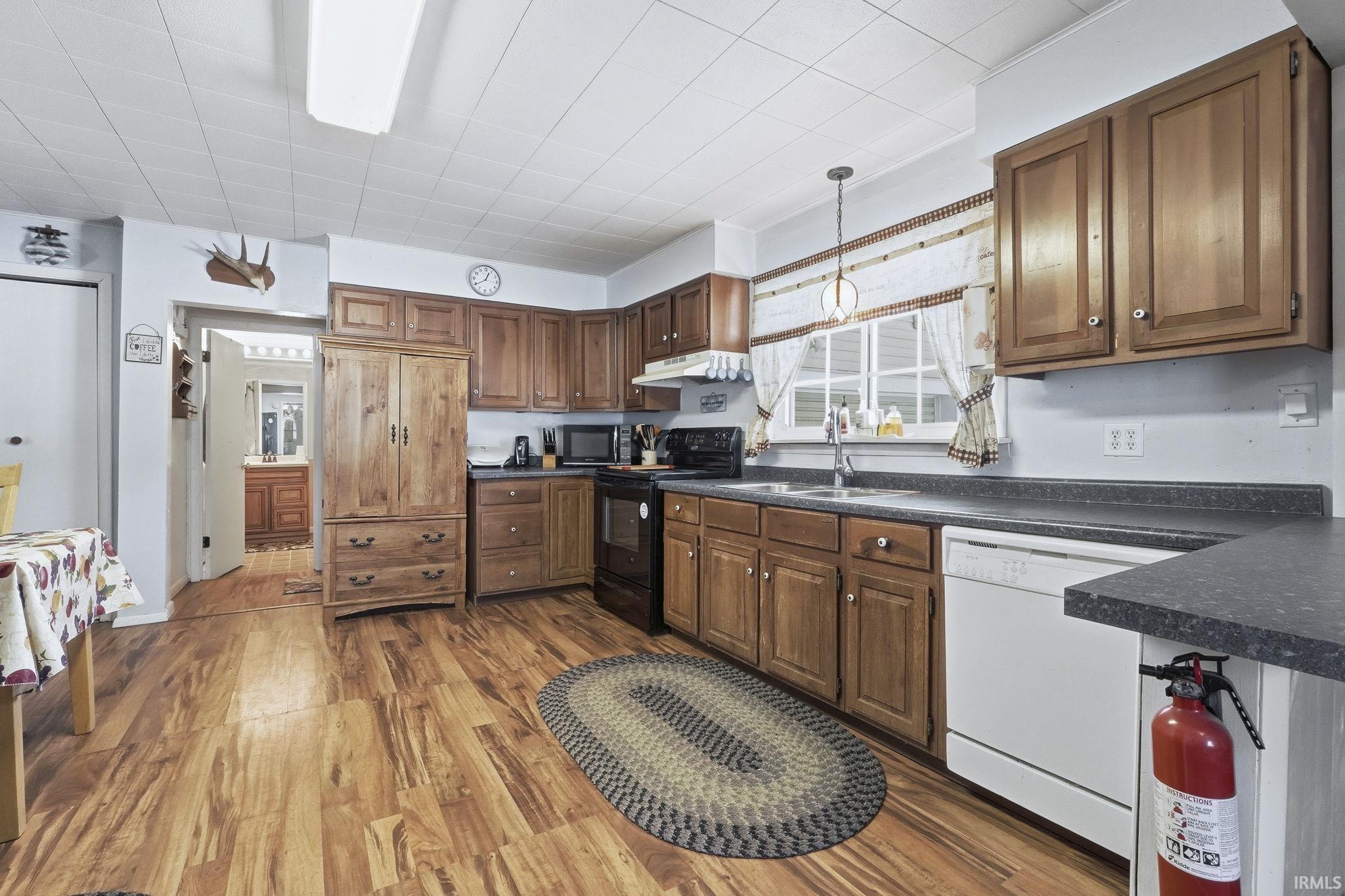 Kitchen with dark countertops, black range with electric cooktop, dark wood-style floors, white dishwasher, and pendant lighting