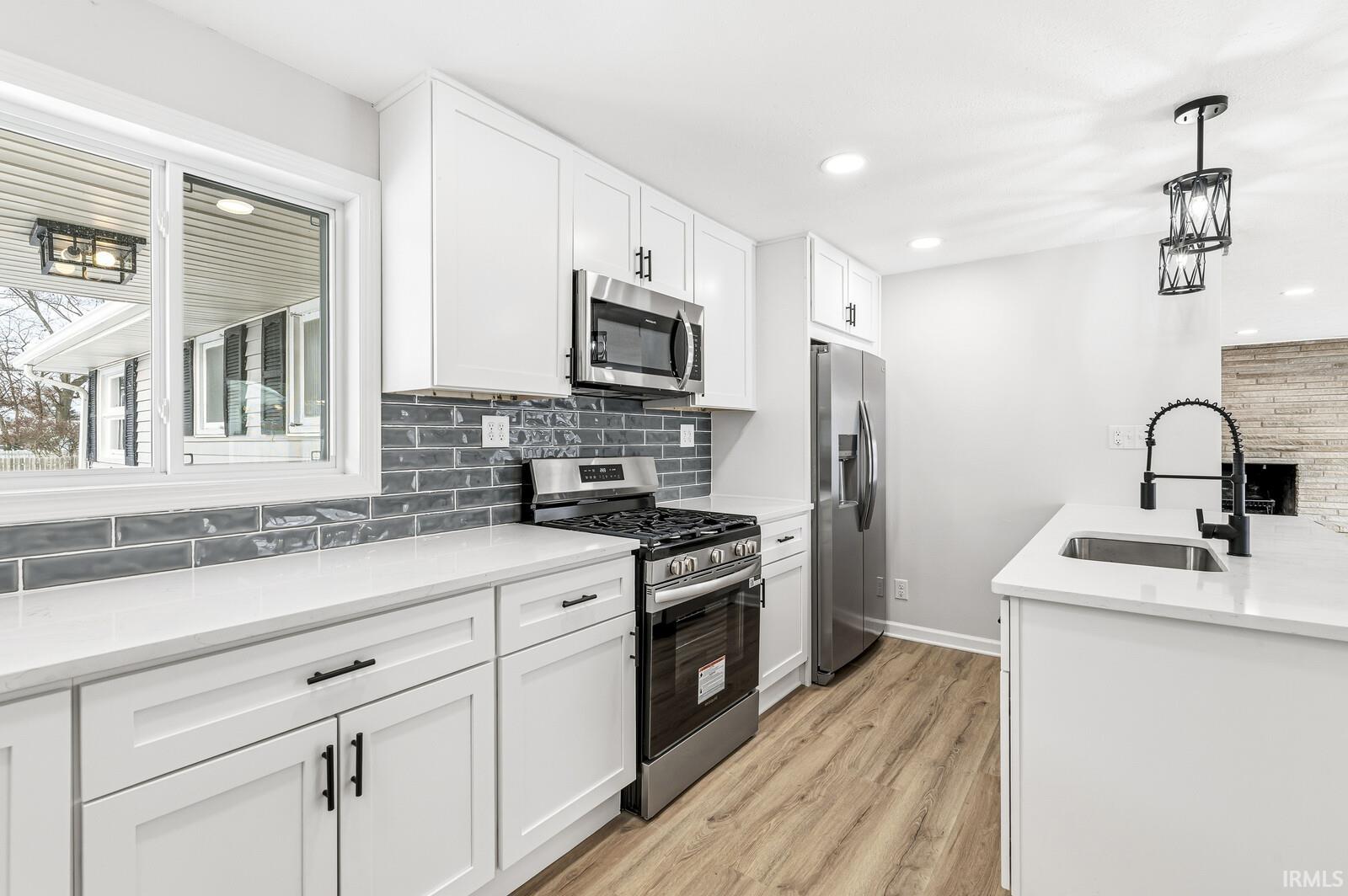 Kitchen with appliances with stainless steel finishes, white cabinetry, light stone counters, hanging light fixtures, and recessed lighting