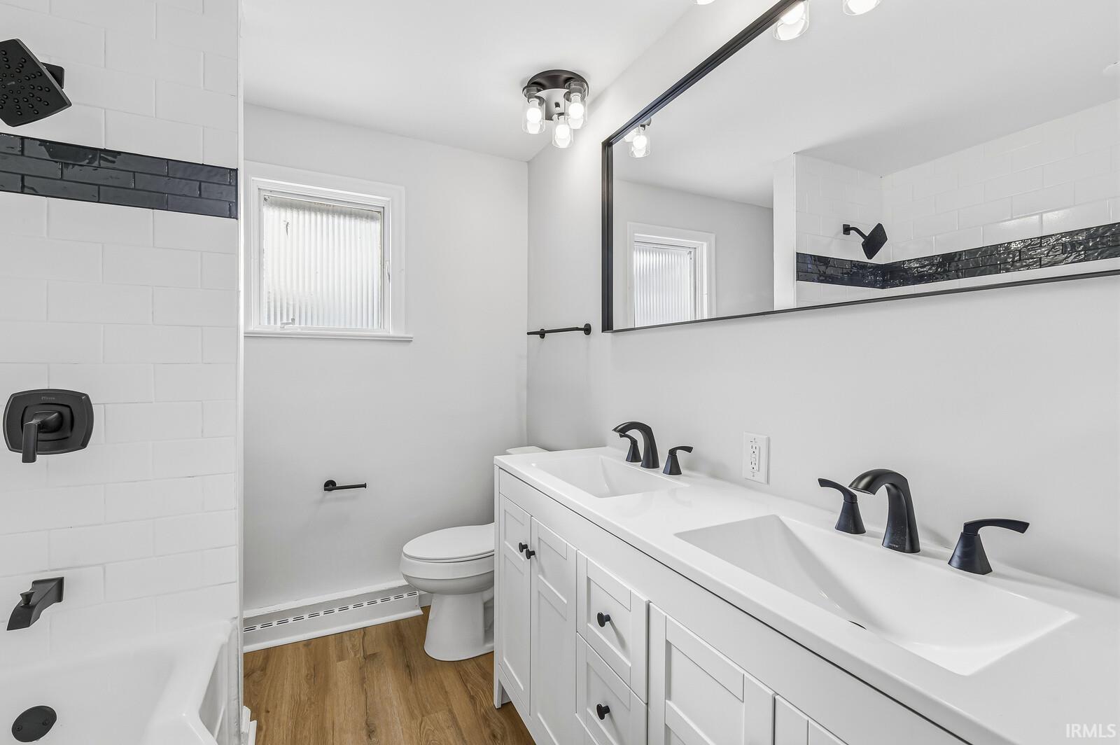 Full bath with double vanity, tiled shower / bath, light wood-type flooring, and a baseboard radiator