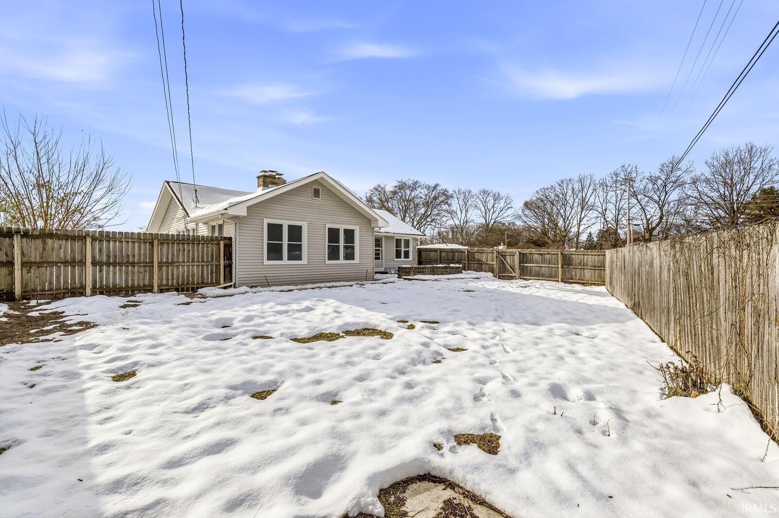 Snow covered rear of property featuring a fenced backyard and a chimney
