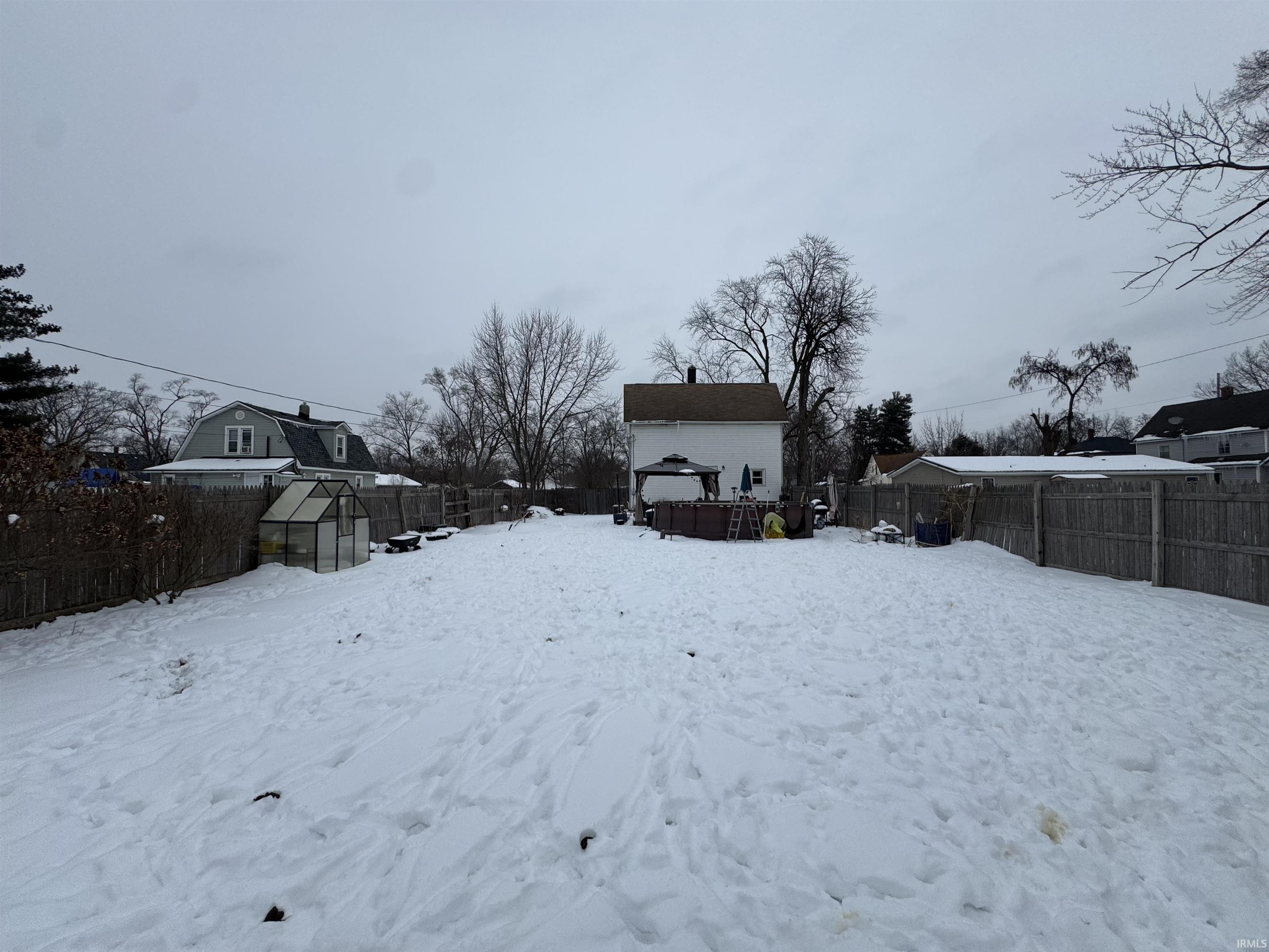 Yard layered in snow featuring a fenced backyard, an outdoor structure, and a greenhouse
