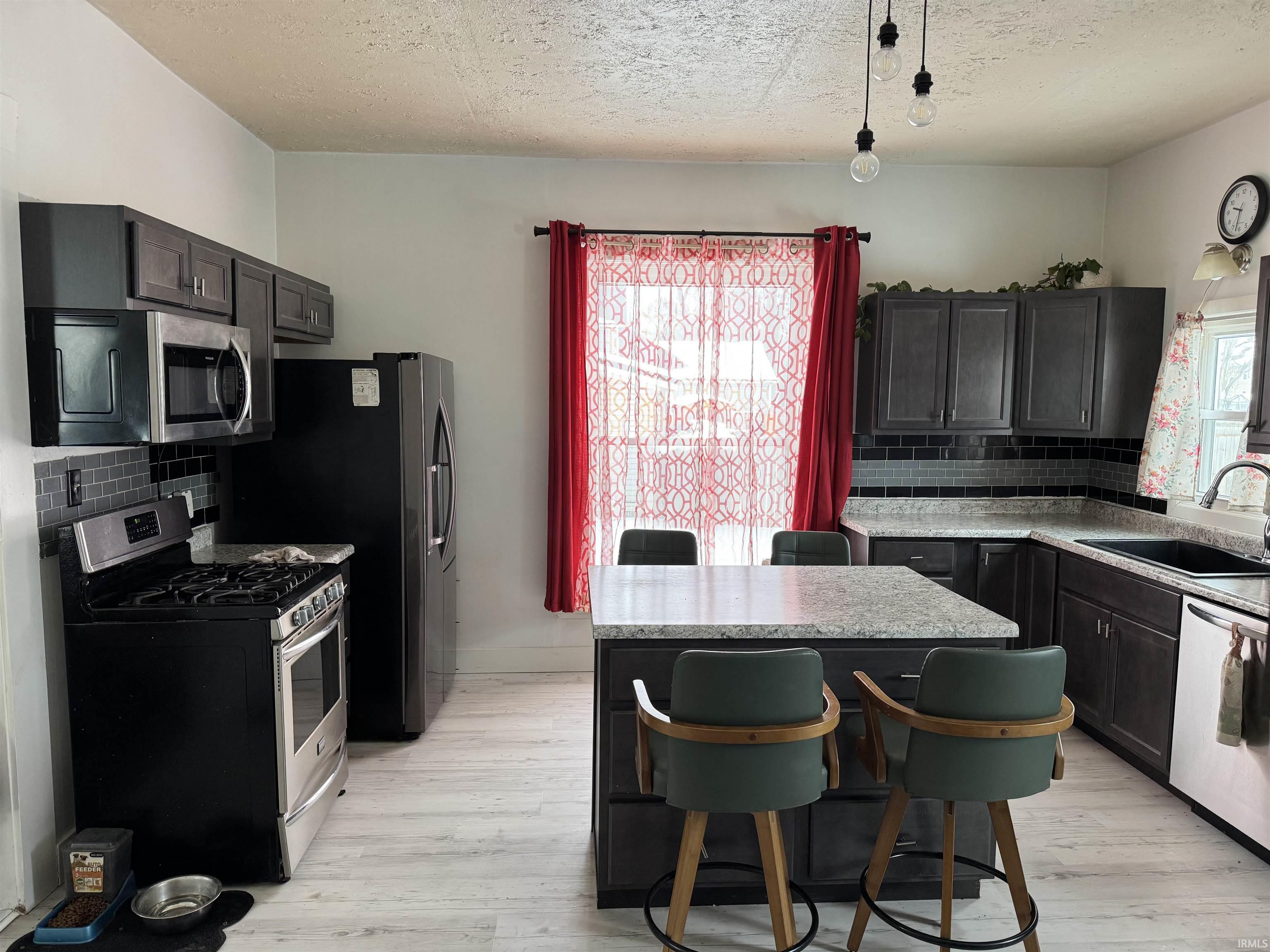 Kitchen featuring backsplash, a breakfast bar, stainless steel appliances, a center island, and a textured ceiling