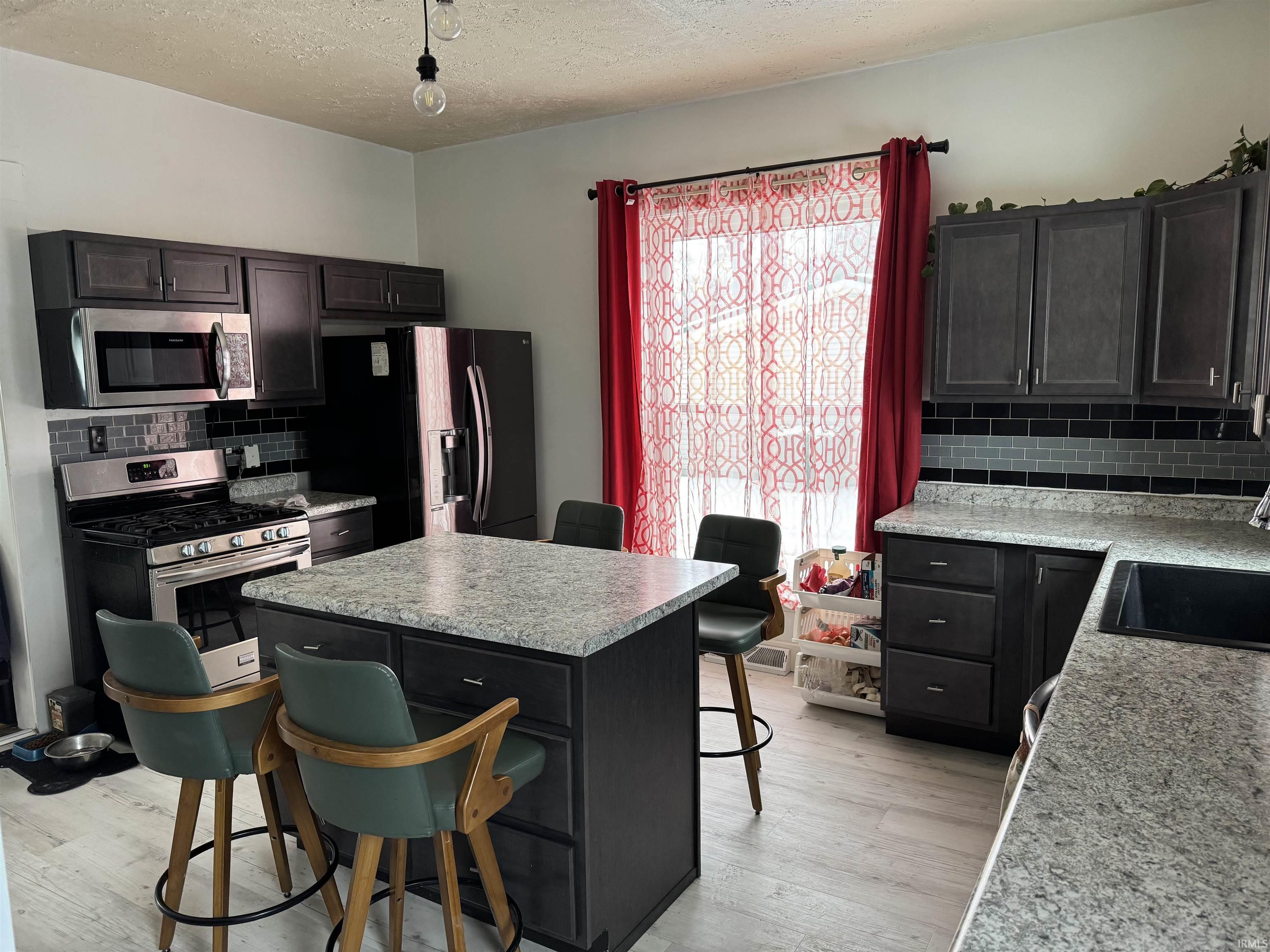 Kitchen featuring a breakfast bar area, decorative backsplash, a center island, stainless steel appliances, and a textured ceiling
