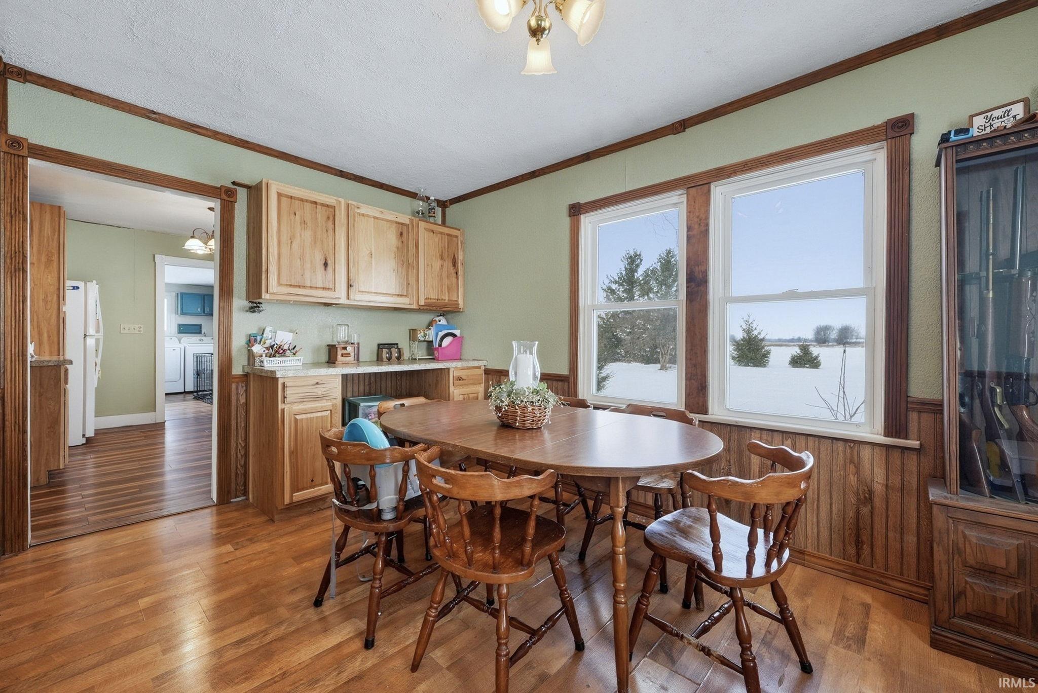 Dining space featuring light wood-type flooring, a wainscoted wall, a textured ceiling, crown molding, and wood walls
