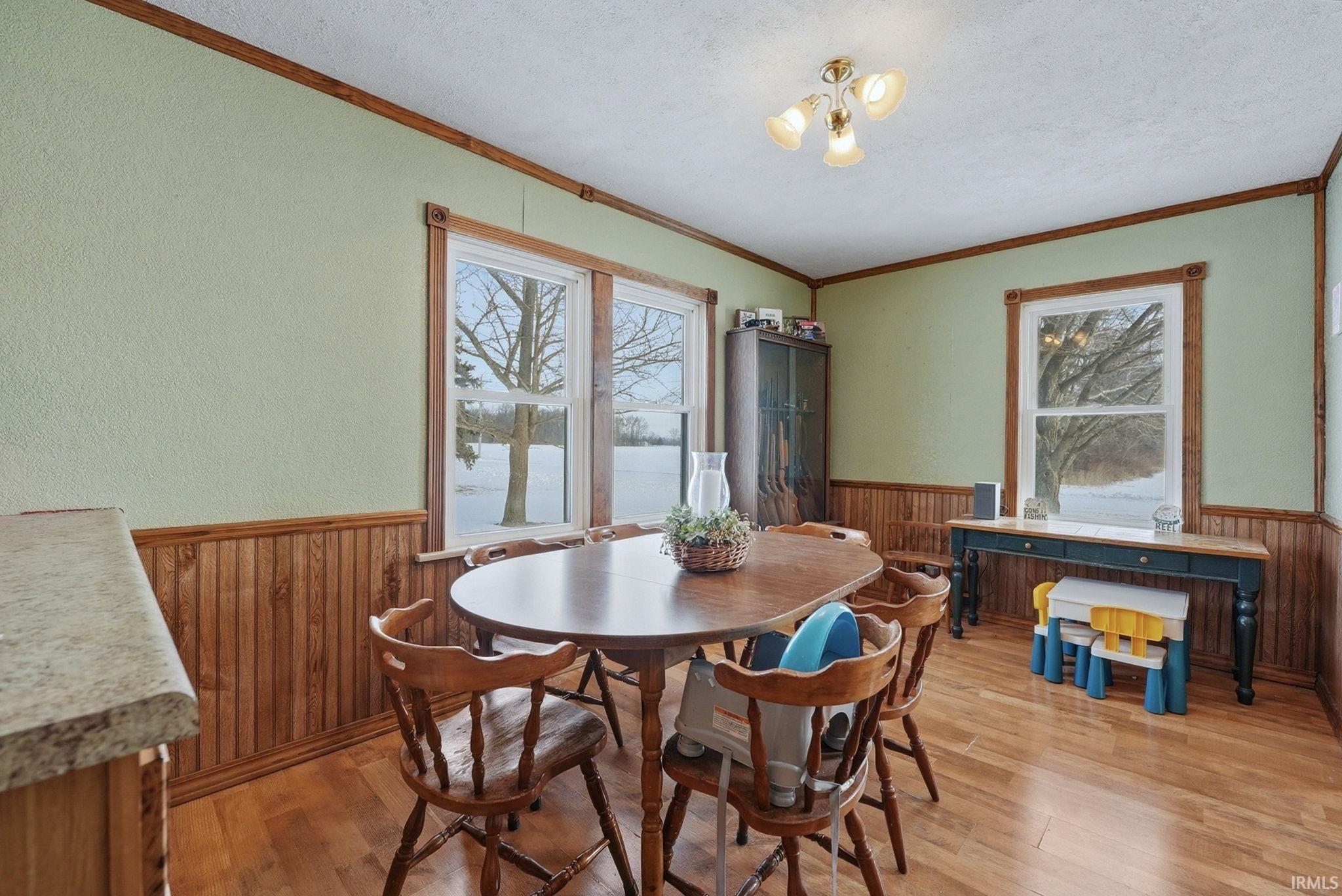 Dining space with wooden walls, a wainscoted wall, crown molding, plenty of natural light, and a textured ceiling