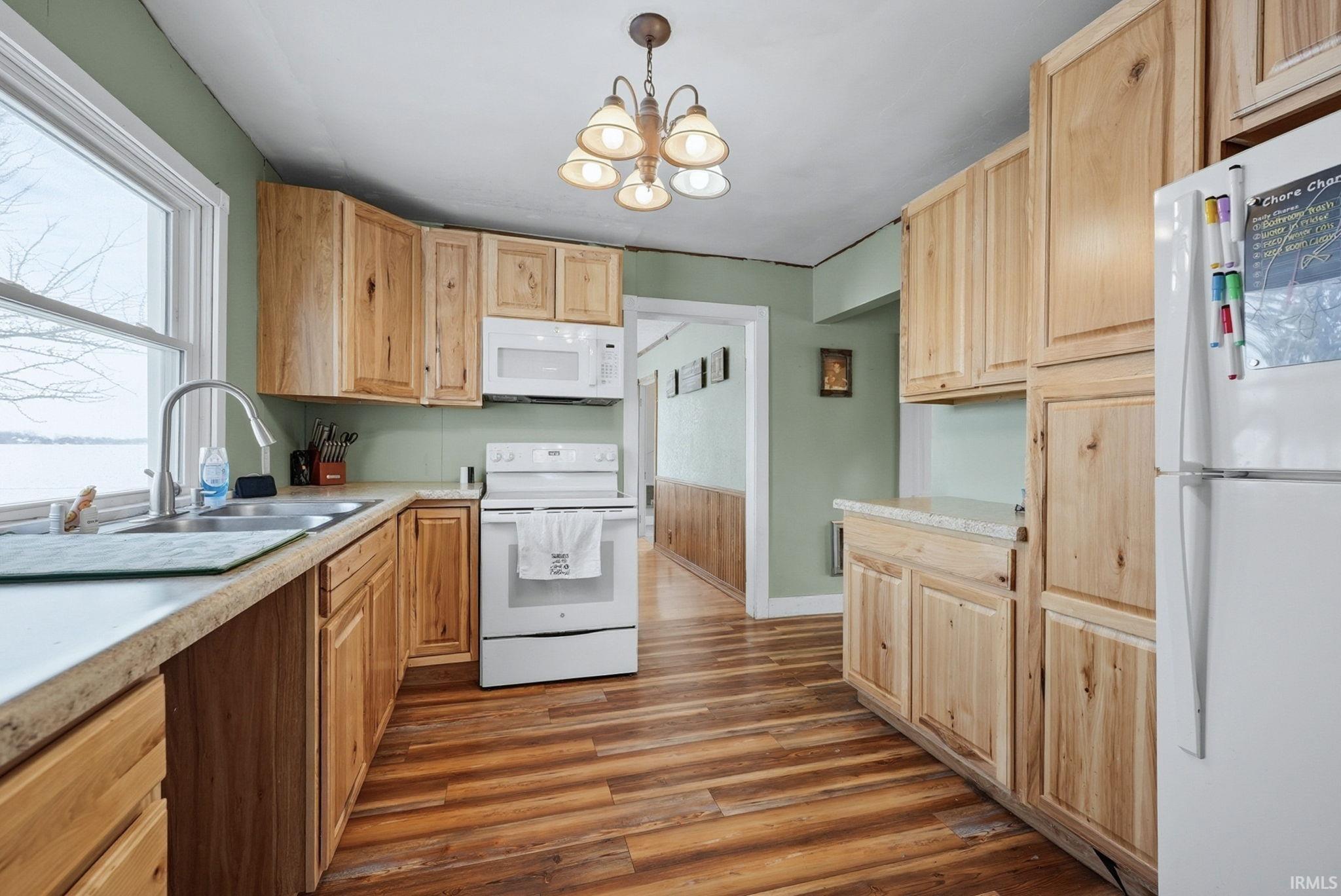Kitchen with white appliances, light wood finish cabinets, light countertops, and dark wood-style flooring