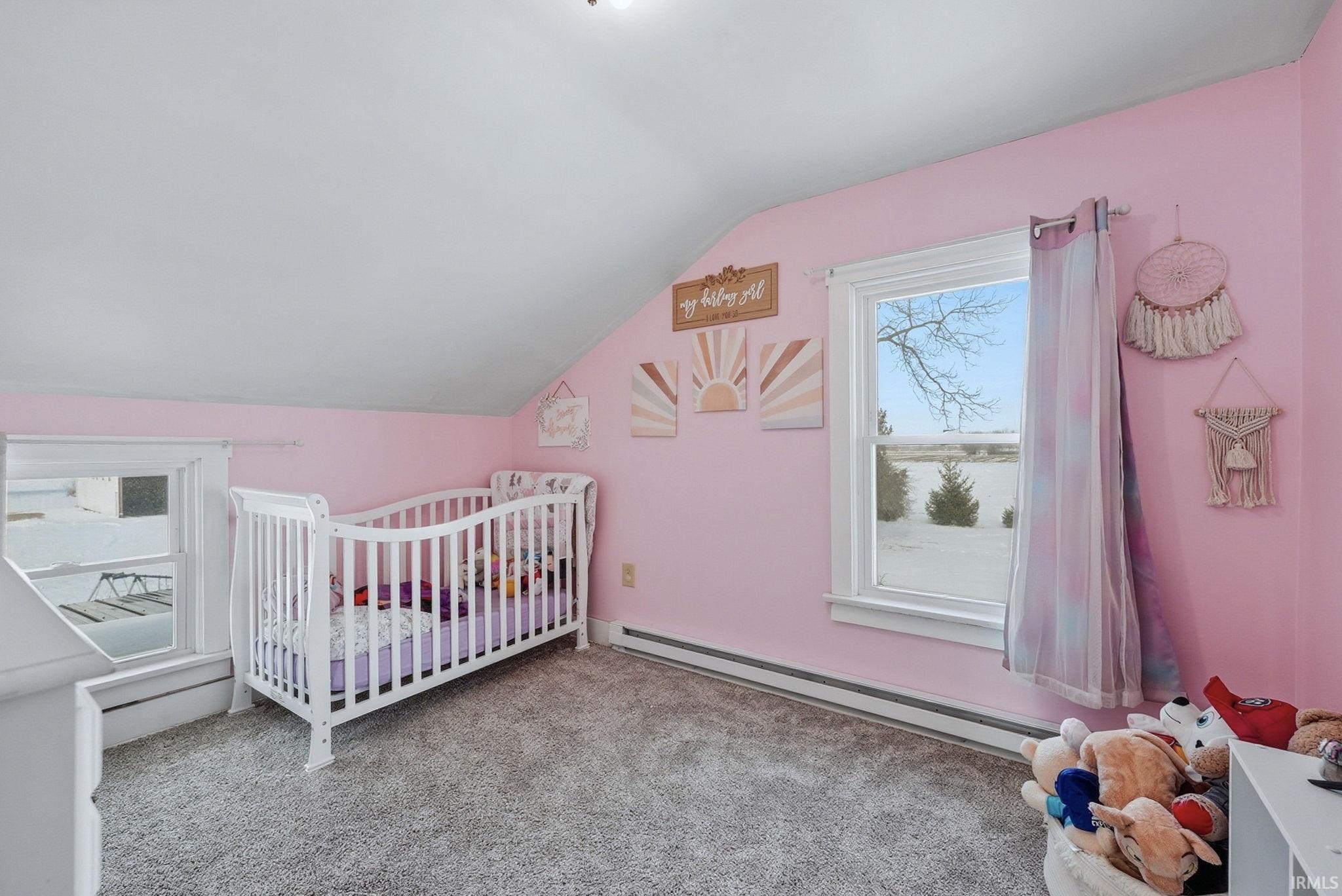 Carpeted bedroom featuring vaulted ceiling, a baseboard heating unit, a crib, and a water view