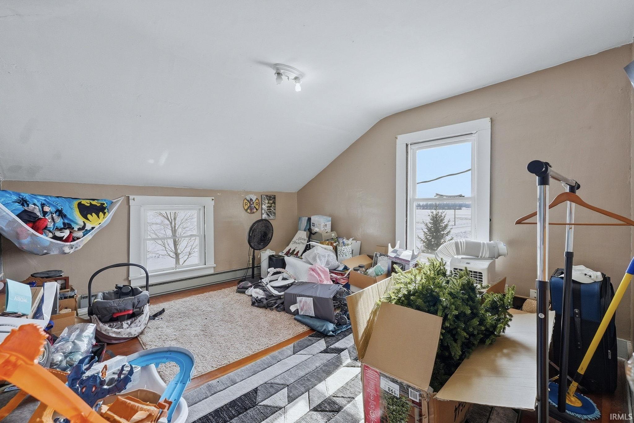 Workout area with vaulted ceiling, plenty of natural light, a baseboard heating unit, and wood finished floors