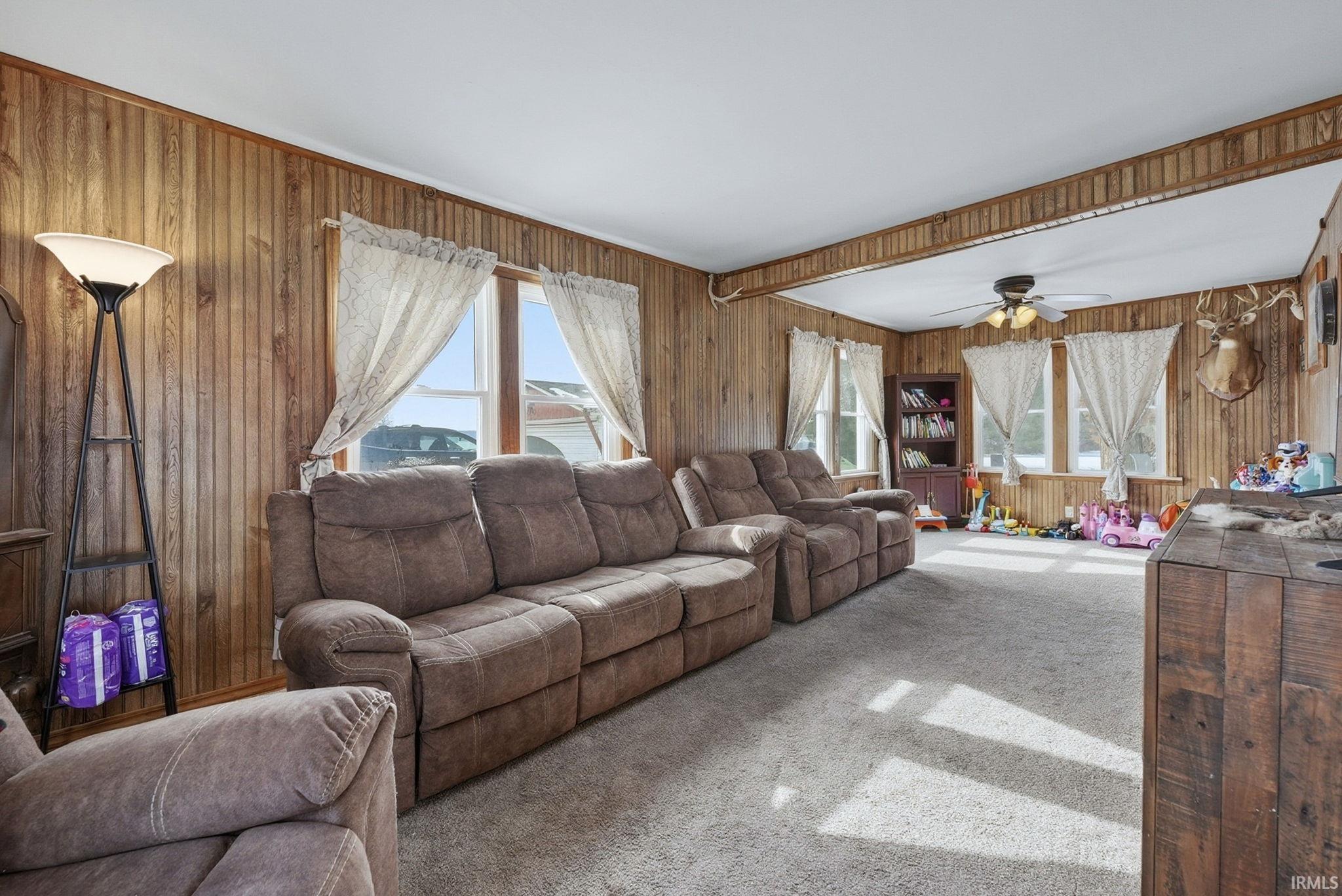 Living room with carpet flooring, healthy amount of natural light, a ceiling fan, and wood walls