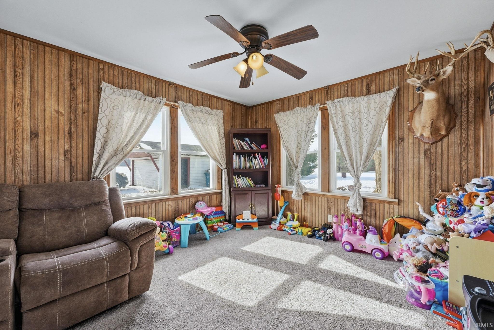 Game room featuring carpet floors, ceiling fan, and wooden walls