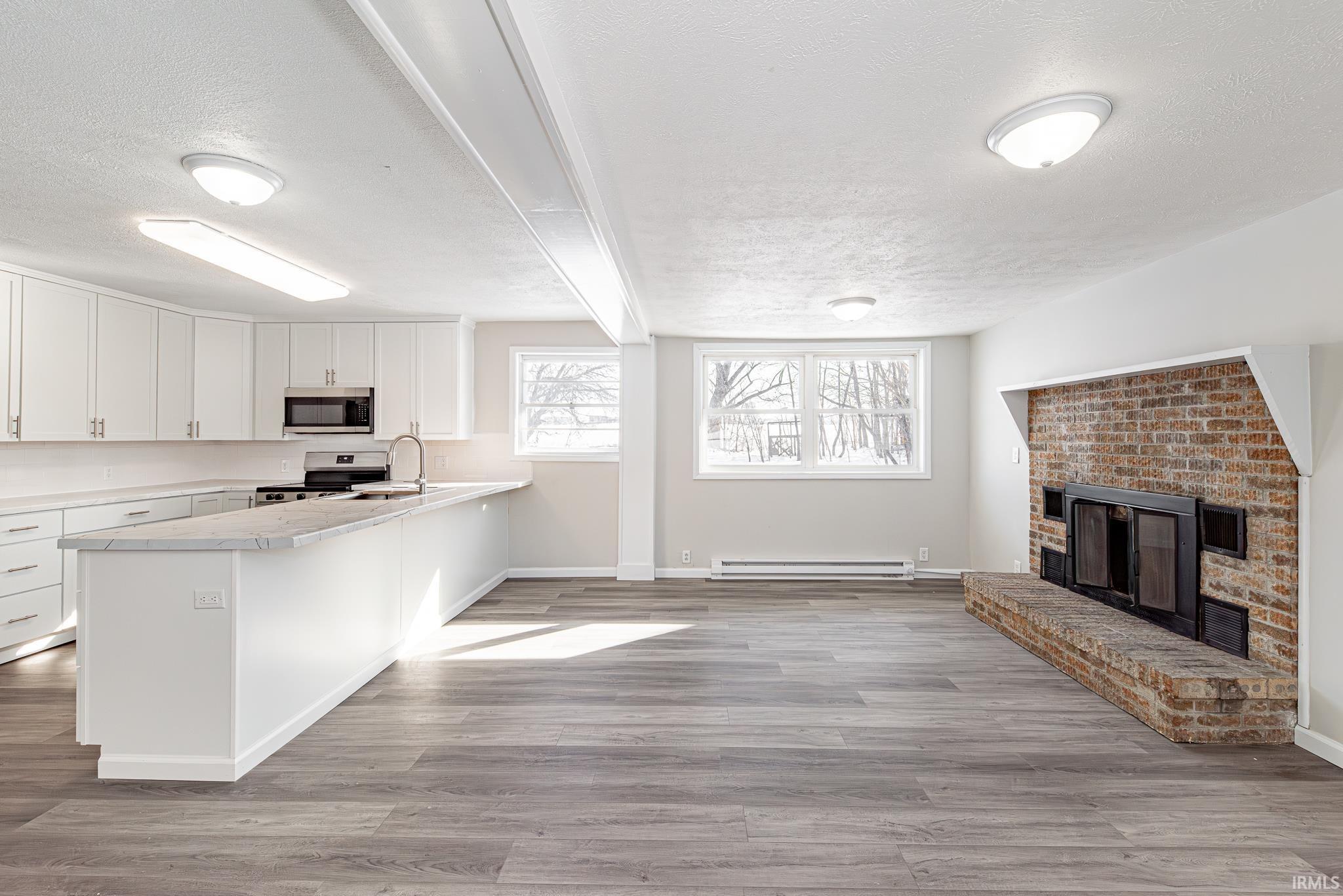 Kitchen with a textured ceiling, a fireplace, white cabinets, open floor plan, and a peninsula