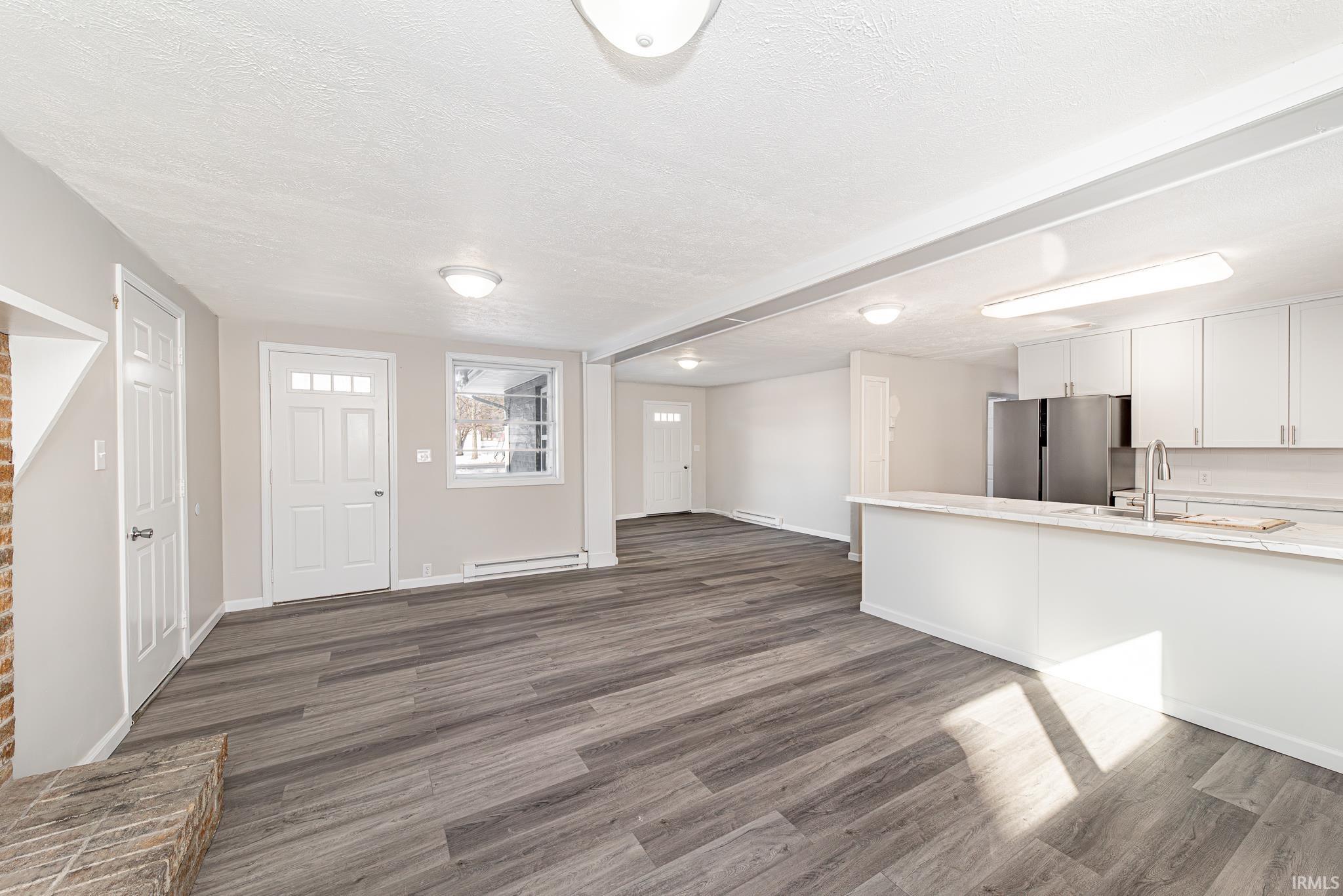 Unfurnished living room with dark wood-style flooring, a textured ceiling, and a baseboard heating unit