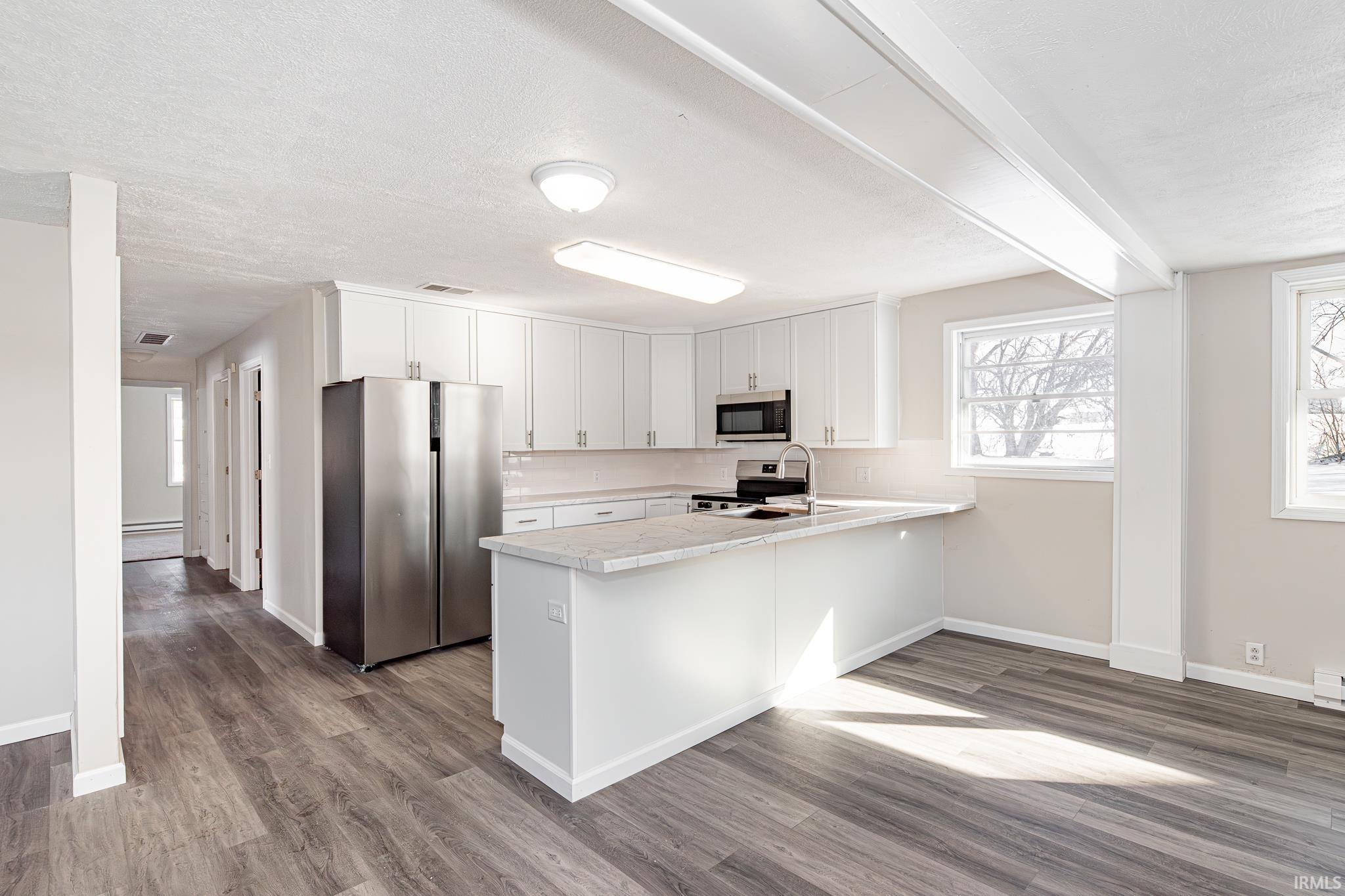 Kitchen featuring stainless steel appliances, white cabinets, dark wood-type flooring, a peninsula, and a textured ceiling